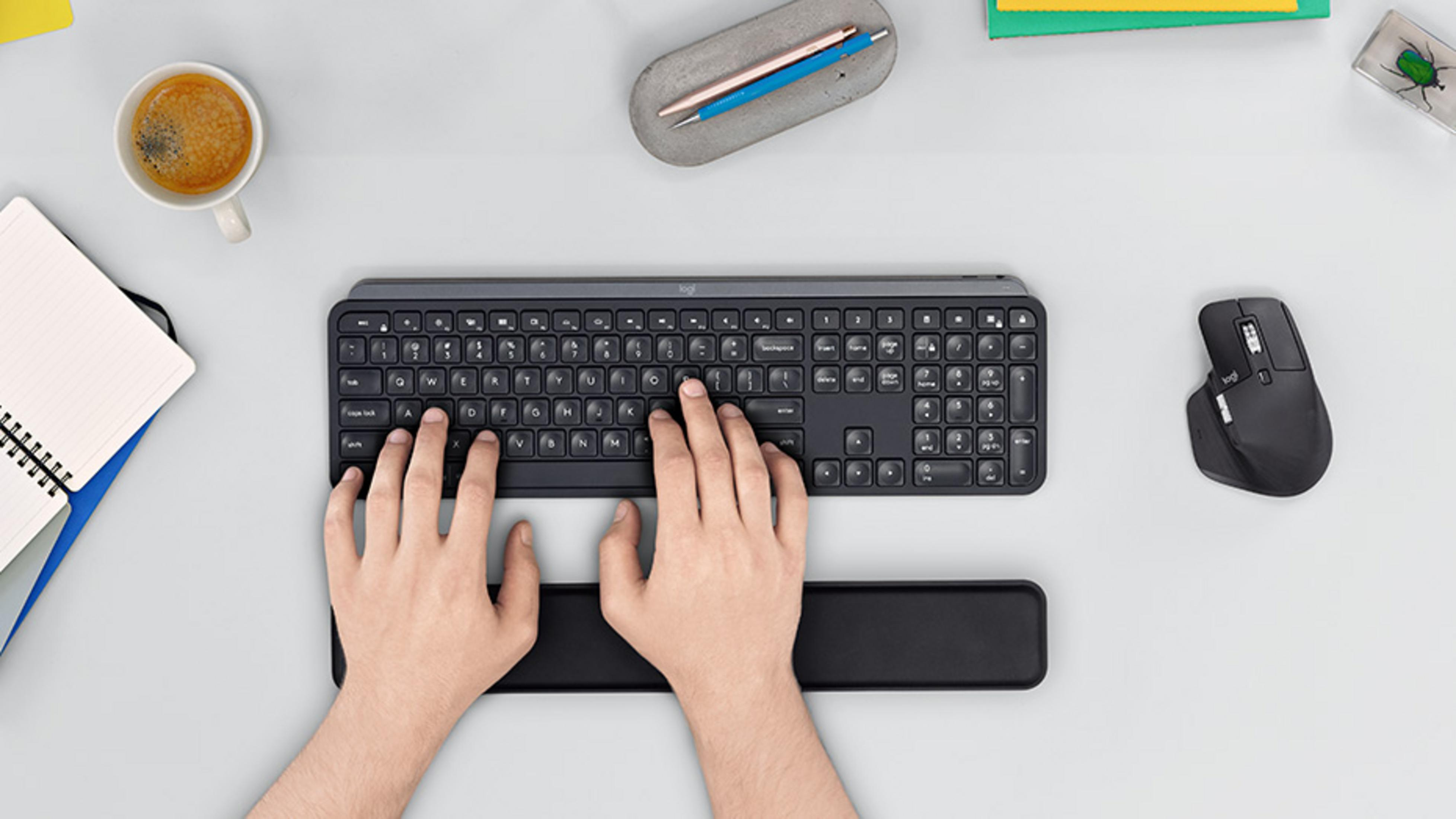 Mani che digitano su una tastiera, con mouse, caffè e taccuino vicini.