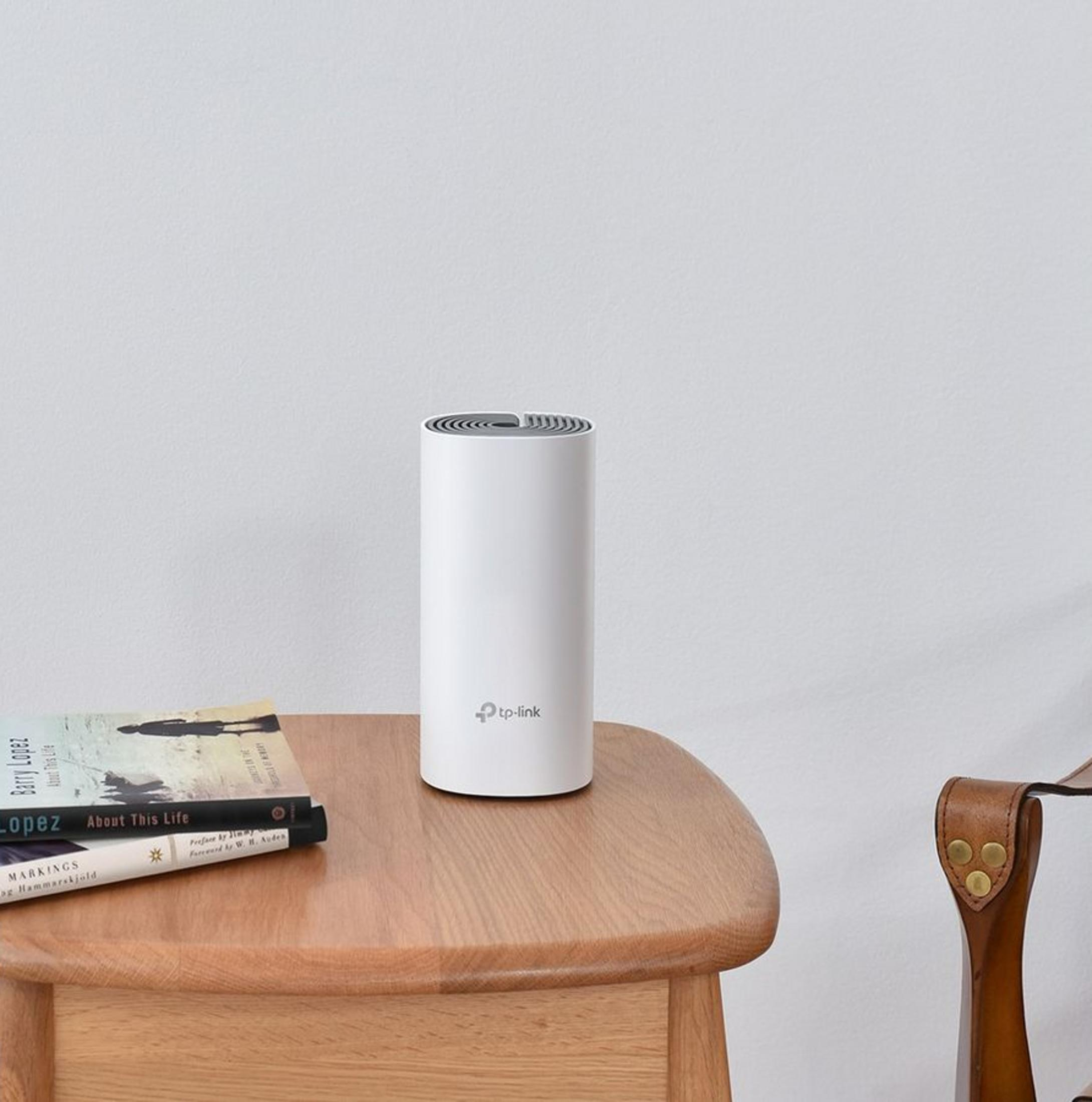 Biały router TP-Link stoi na drewnianym stole obok książek i krzesła.