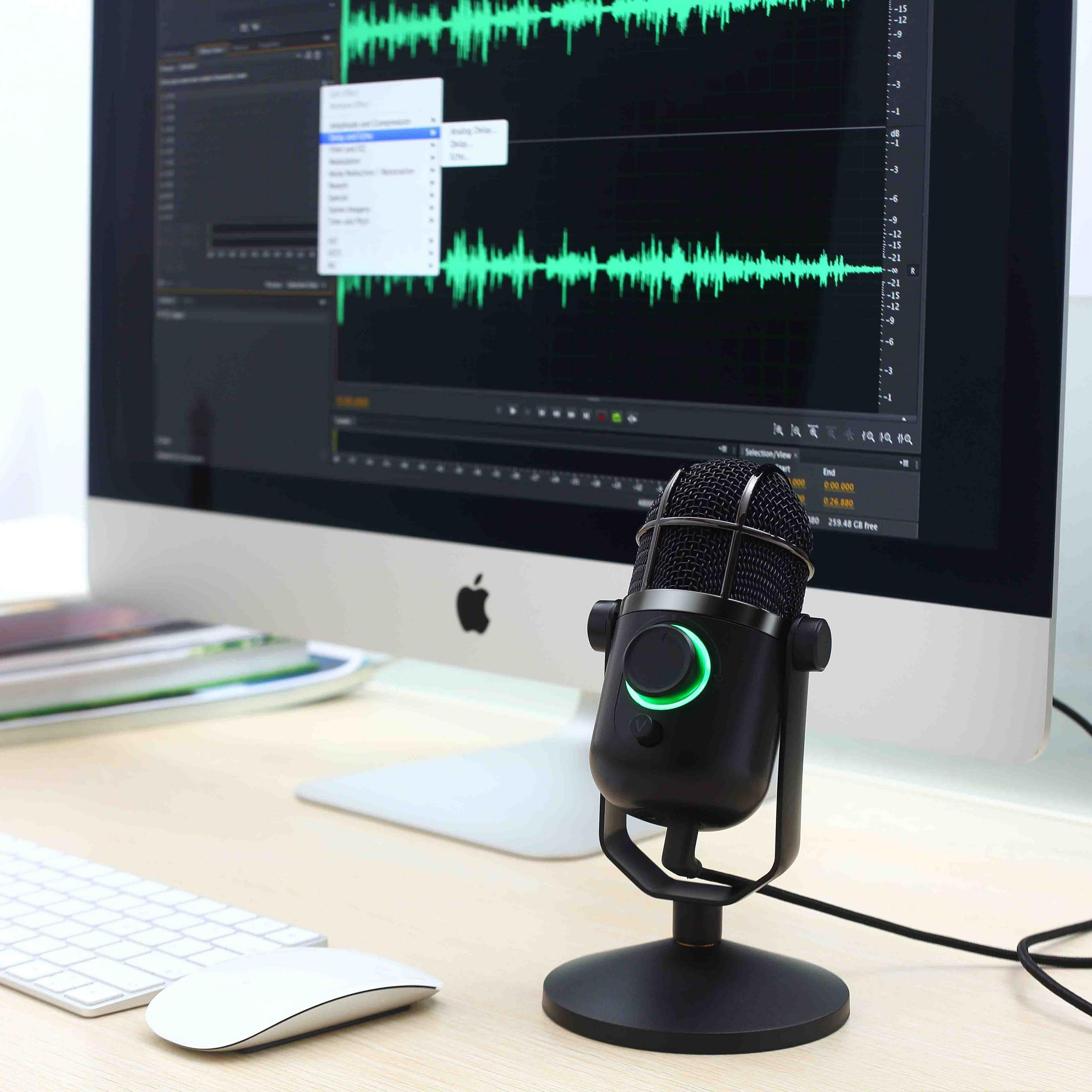 Un microfono nero davanti a uno schermo di computer che mostra forme d'onda audio.