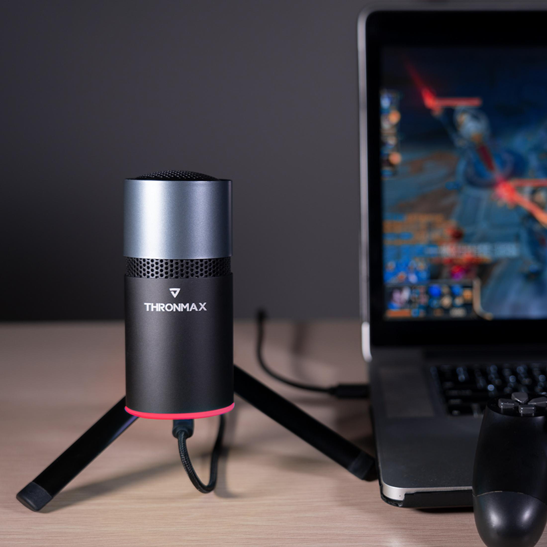 Un microfono su treppiede accanto a un laptop e un controller di gioco.