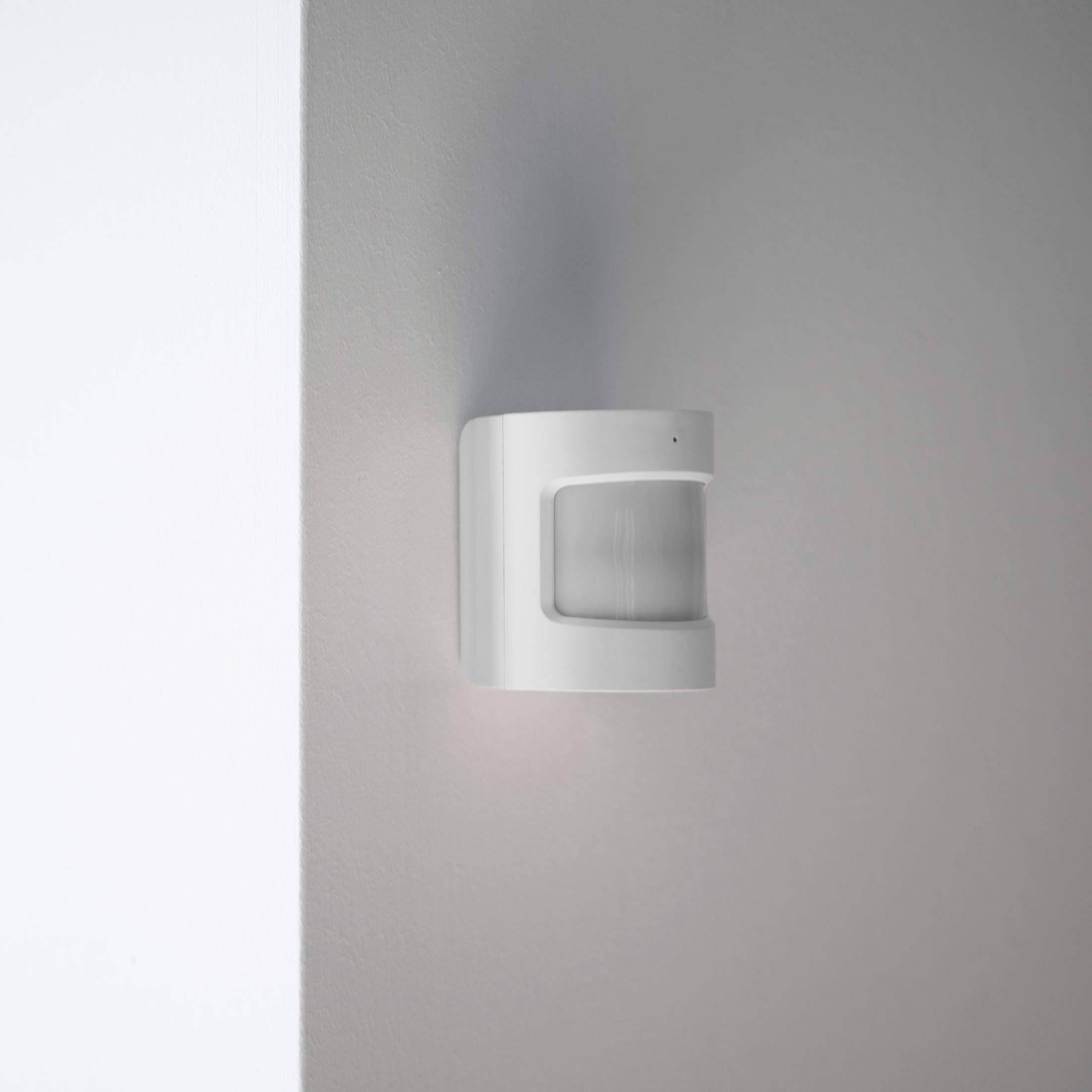 Un rilevatore di movimento bianco montato su un muro grigio.