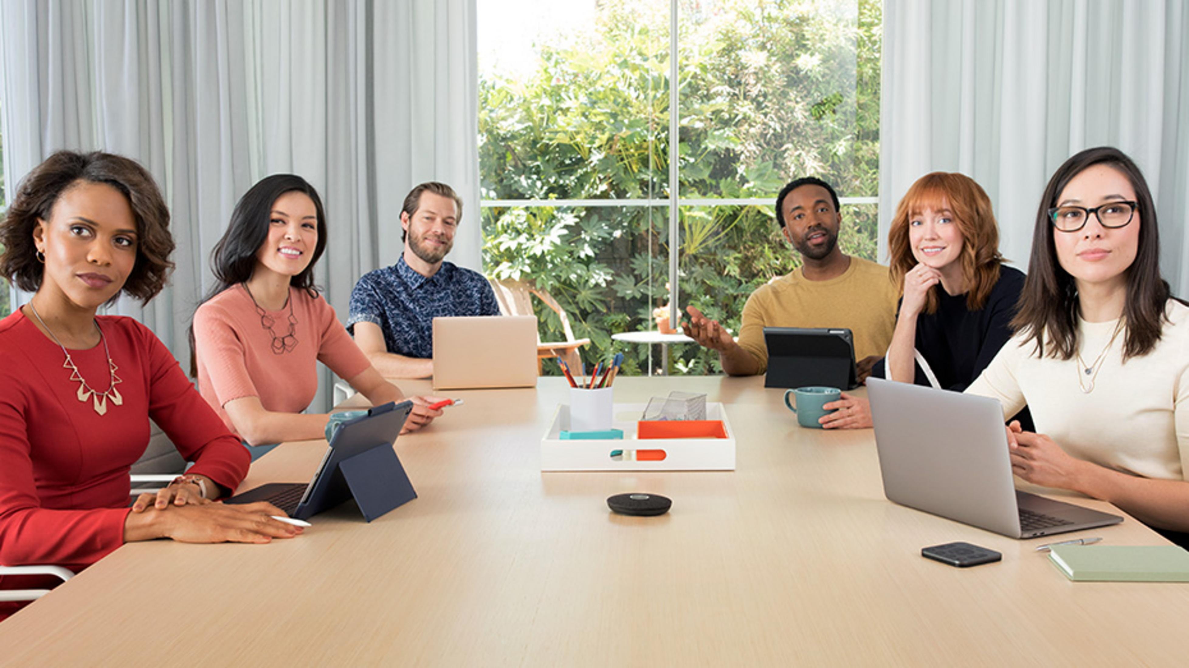 Ludzie siedzą przy stole z laptopami i tabletami.