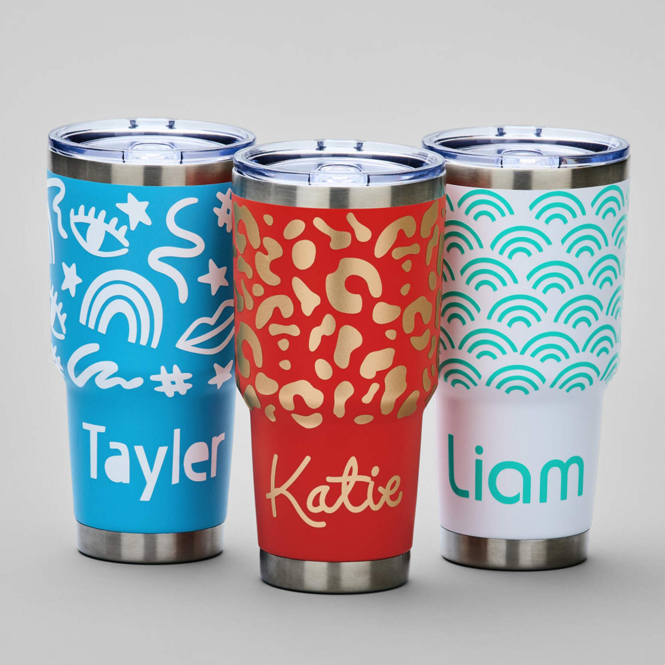 Drei personalisierte Becher: blau mit weißen Zeichnungen, rot mit goldenem Leopardenmuster, weiß mit teal Wellen.