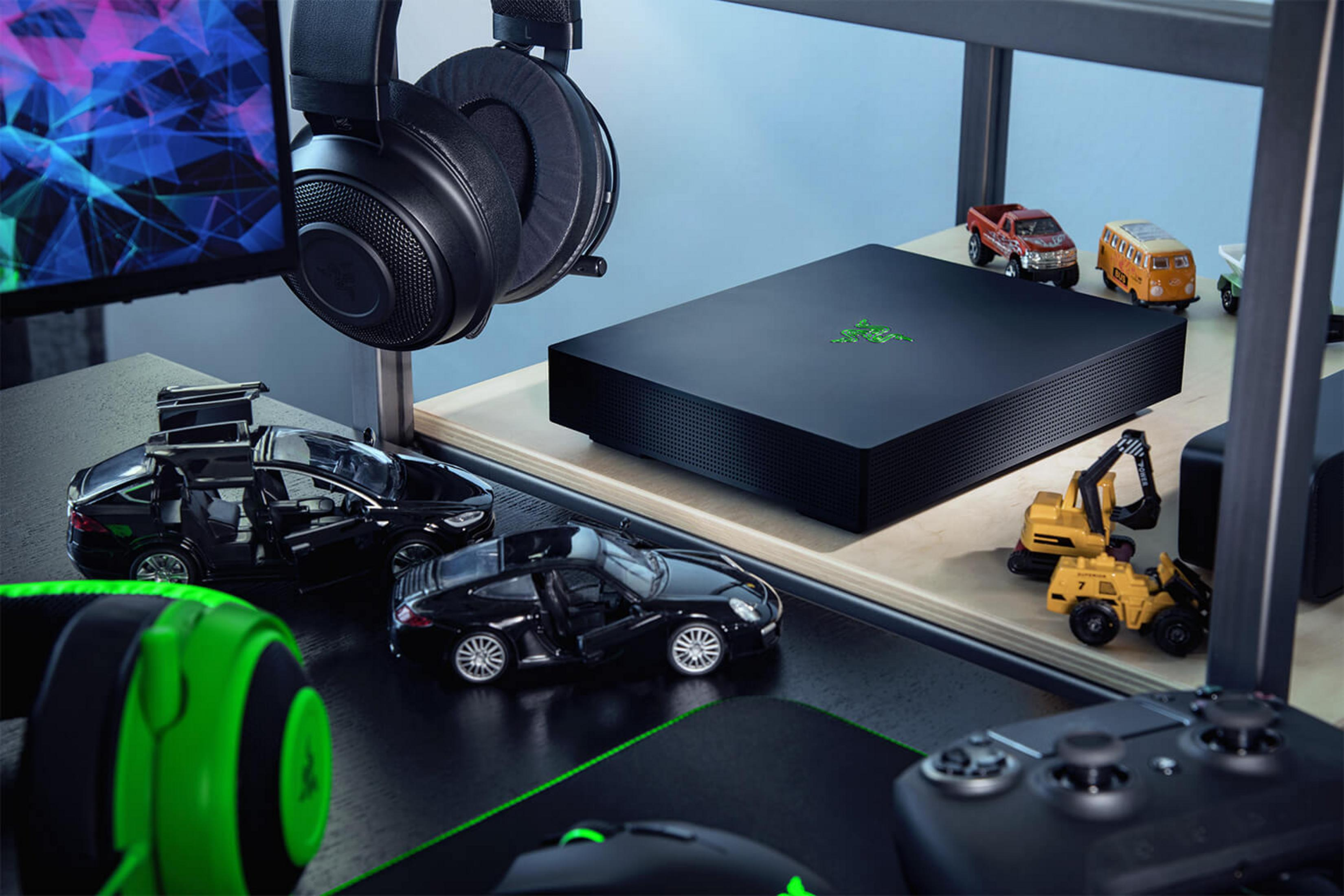 Czarna konsola Razer, słuchawki i zabawki samochodziki na biurku. Kontroler w zestawie.