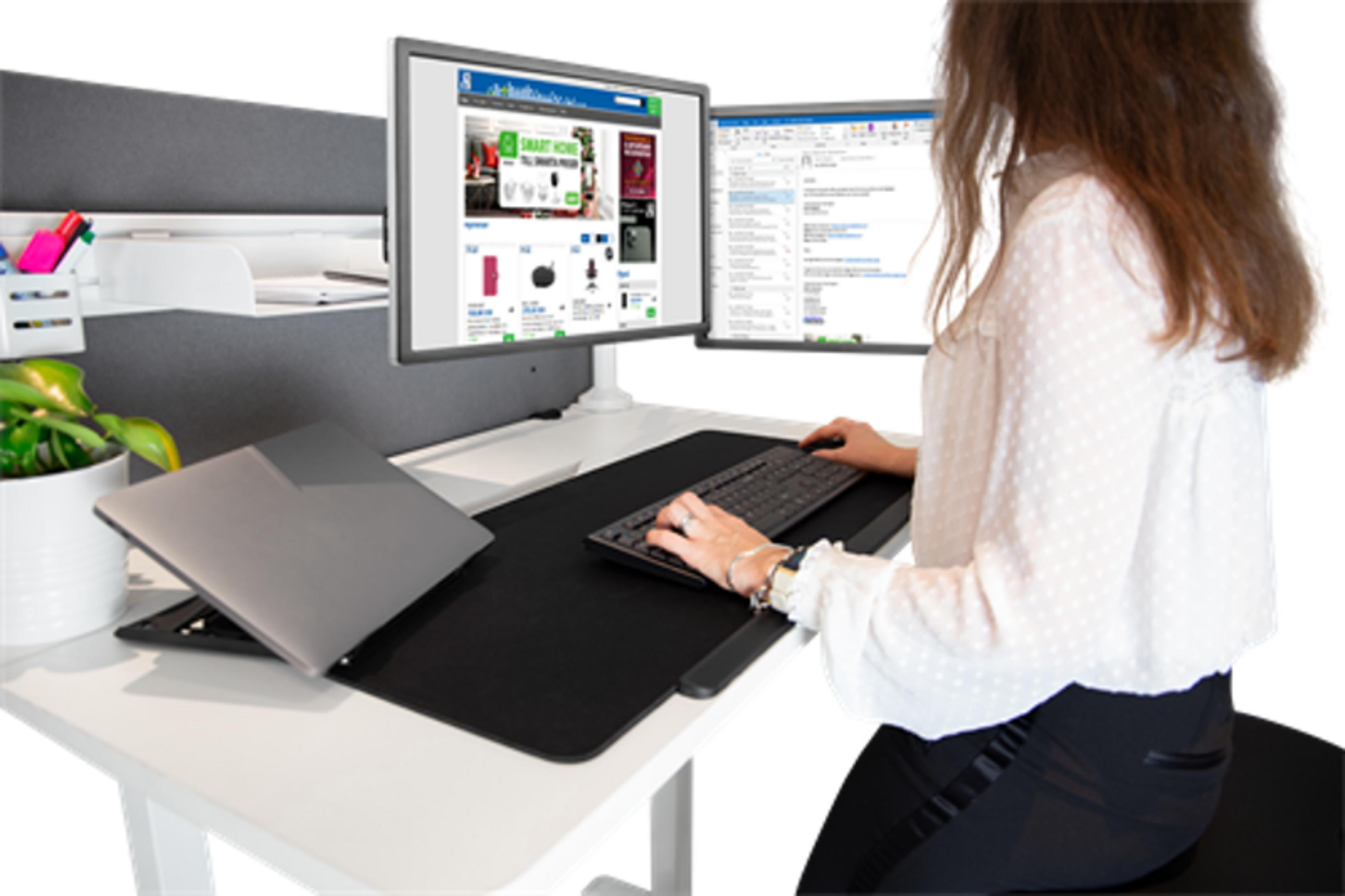 Eine Frau tippt auf einer Tastatur vor zwei Monitoren in einem modernen Büro.
