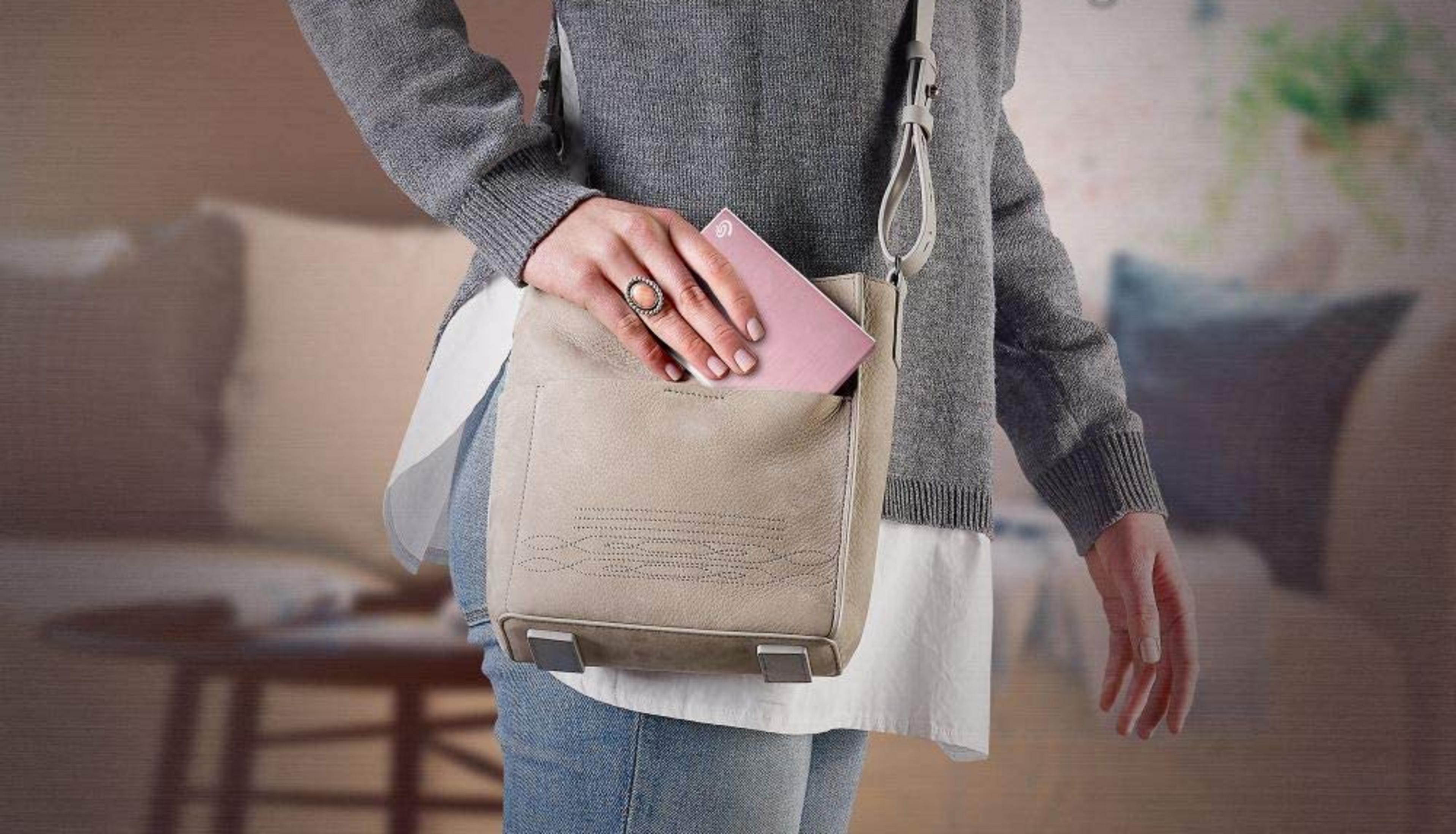 Osoba wkłada różowe urządzenie do beżowej torebki. Rozmyte tło.