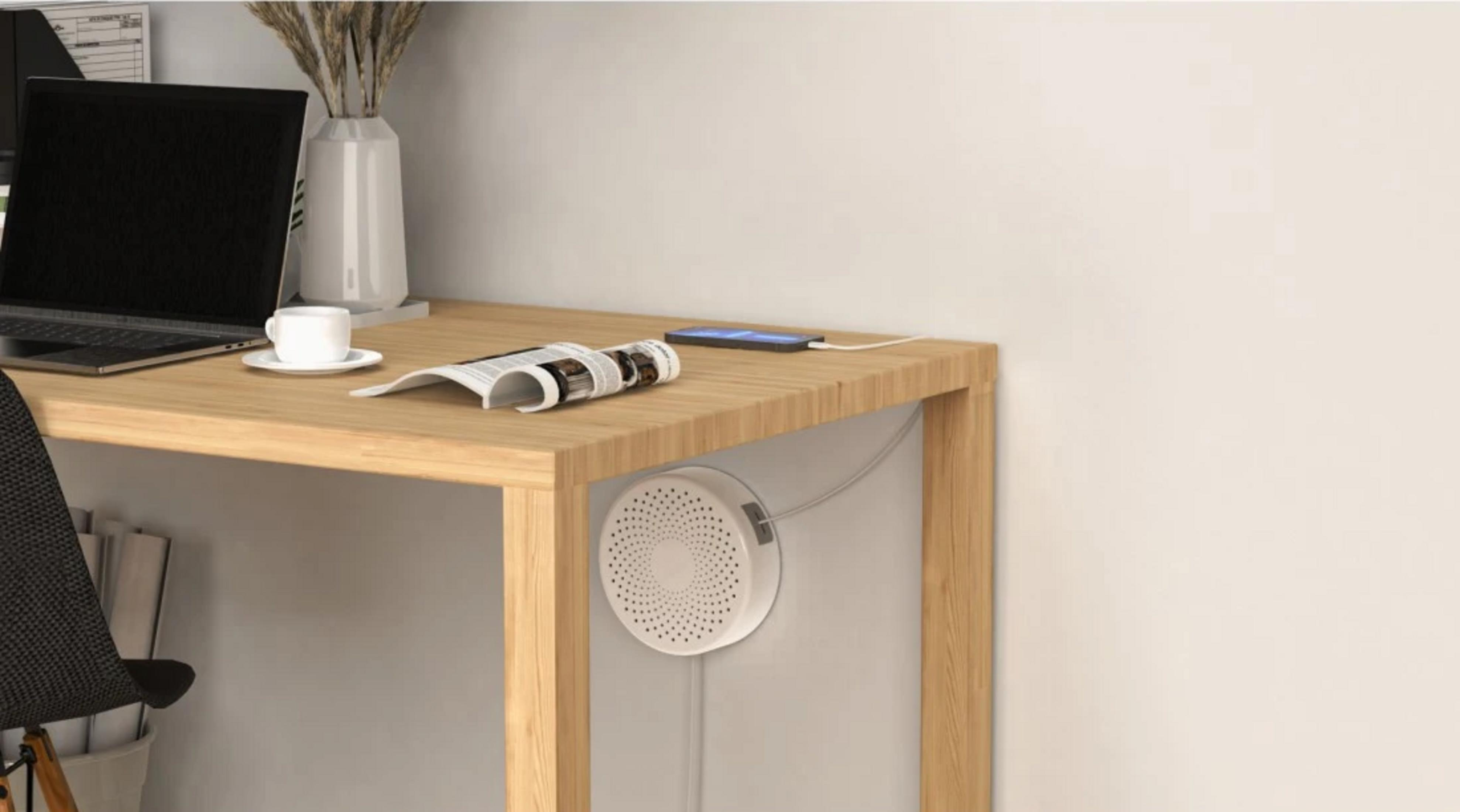 Scrivania in legno con laptop, tazza da caffè, rivista, telefono e un dispositivo circolare bianco.