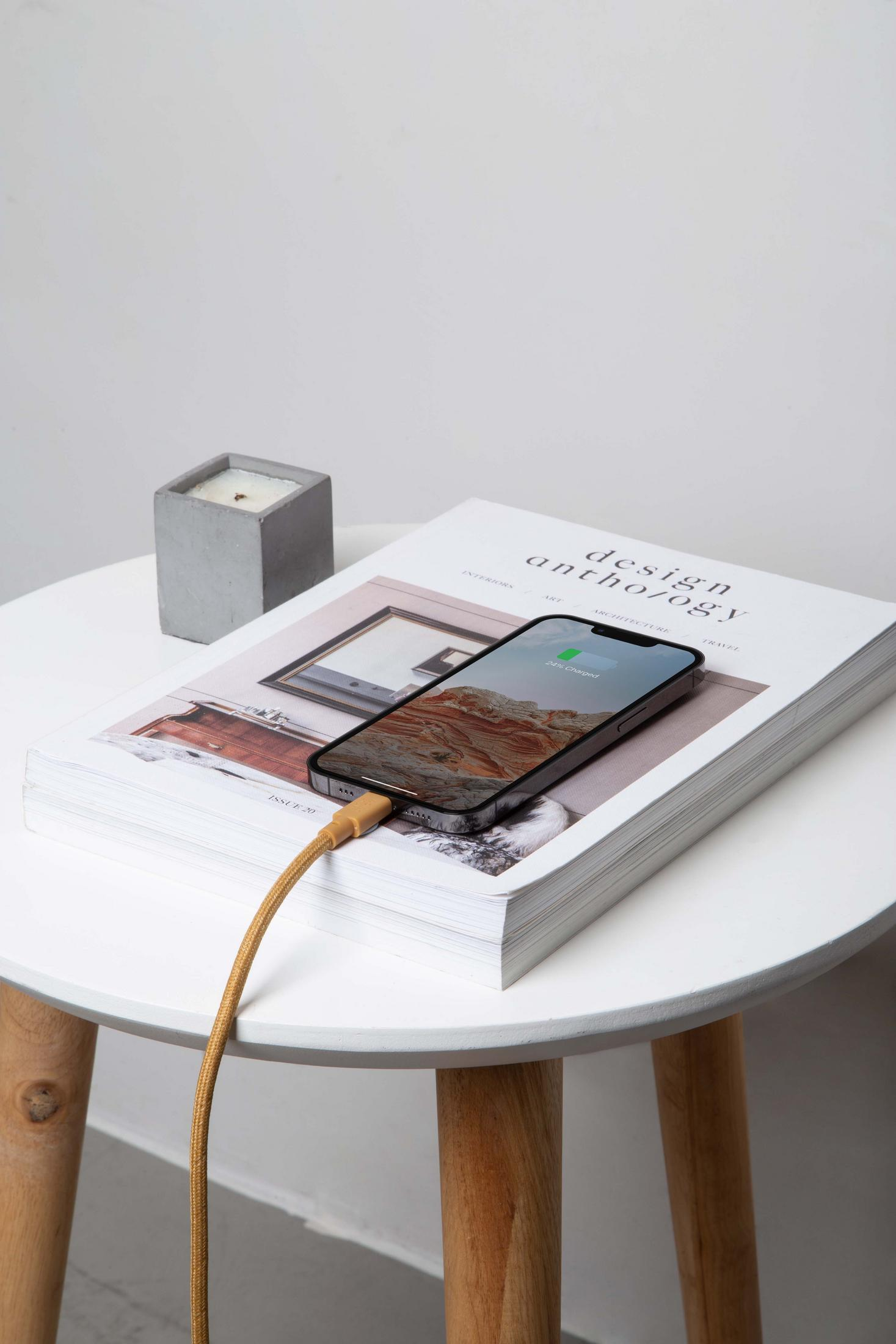 Ein Smartphone lädt auf einem Buch auf einem weißen Tisch, daneben eine Kerze.