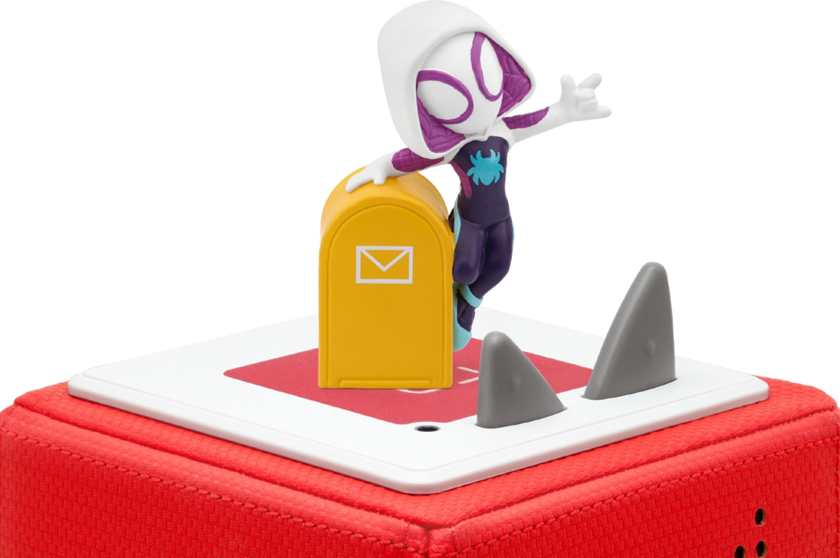 Gwen Stacy Figur auf gelber Postbox mit Haifischflossen auf rotem Sockel.