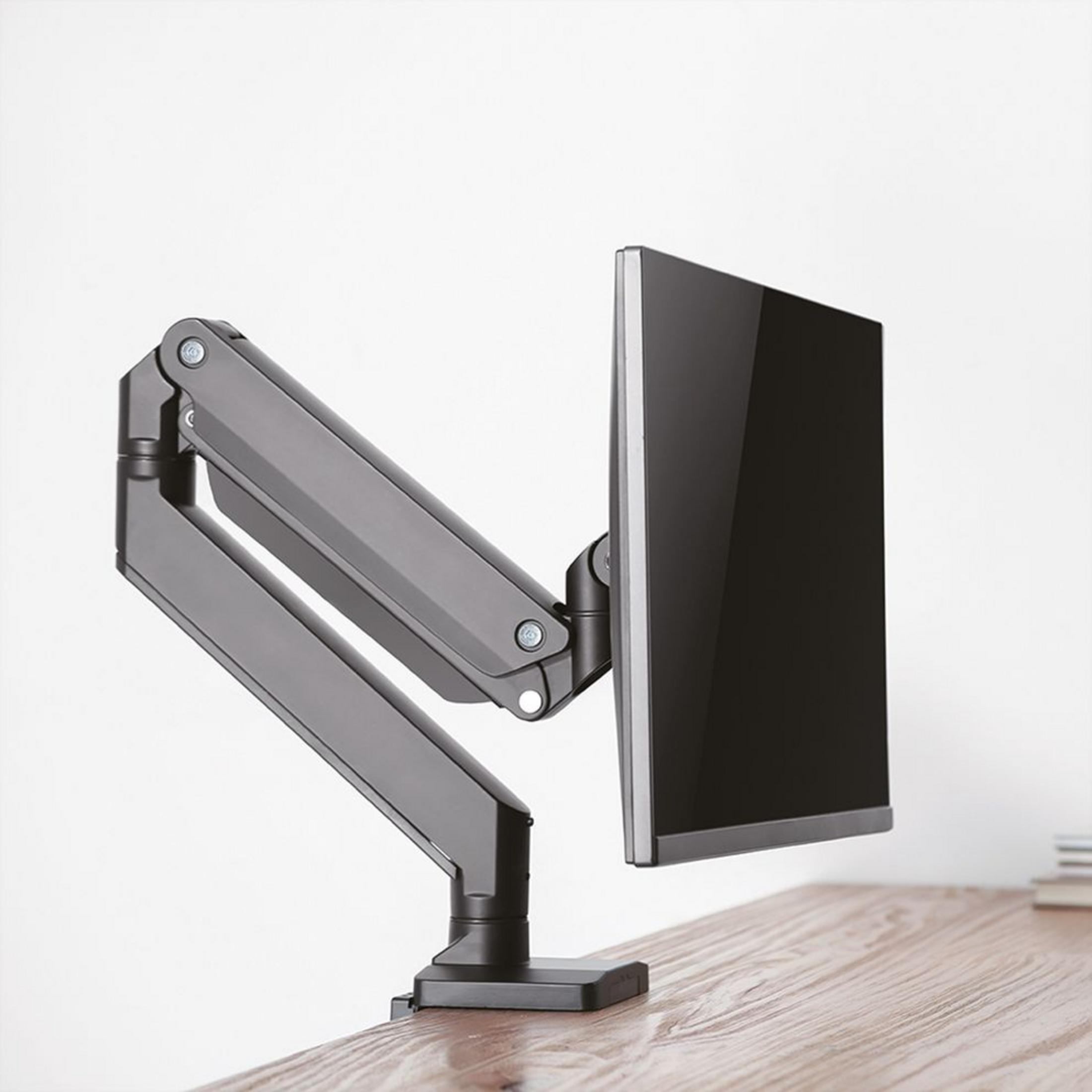 Ein Monitorarm aus Metall hält einen schwarzen Monitor über einem Holztisch.