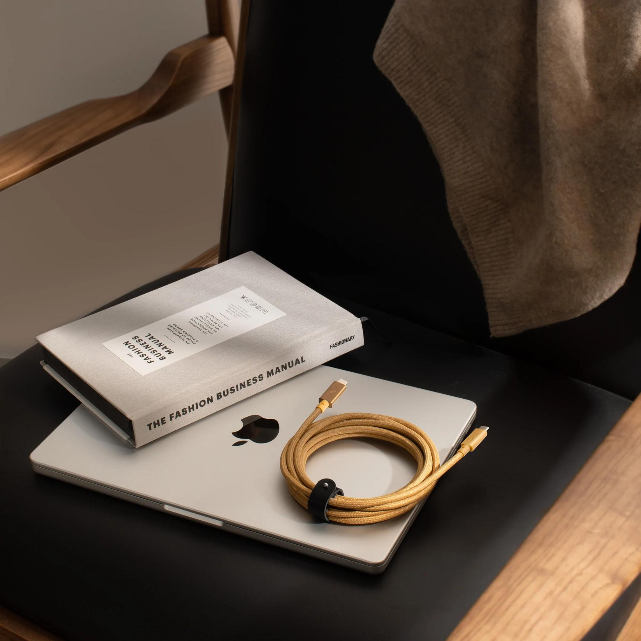 Un MacBook riposa su una sedia accanto a un libro e un cavo di ricarica.