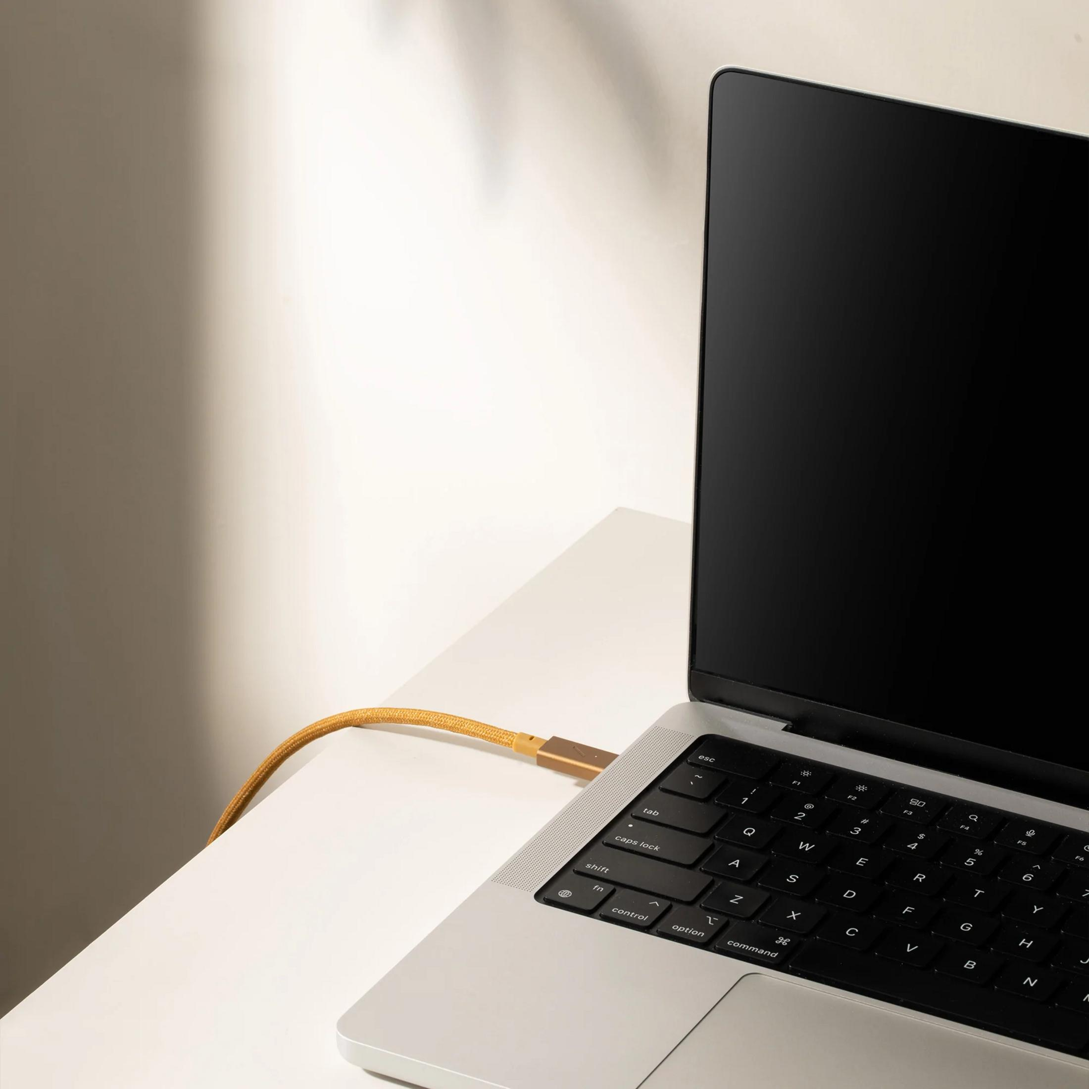 Un cavo di ricarica dorato si collega a un laptop argentato su una scrivania bianca.