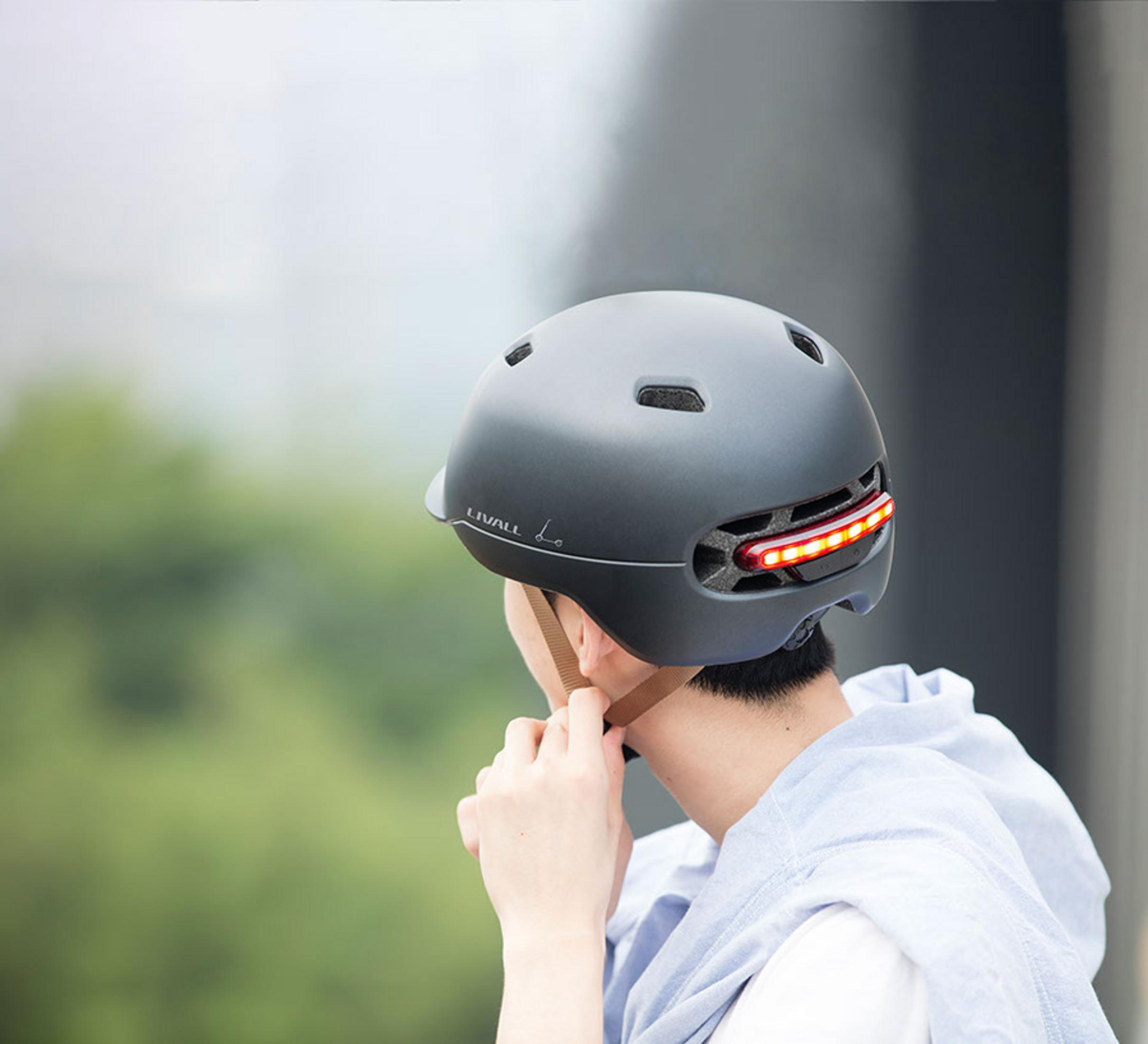 Ein Mann trägt einen grauen Helm mit roten Rückleuchten. Er passt ihn an.