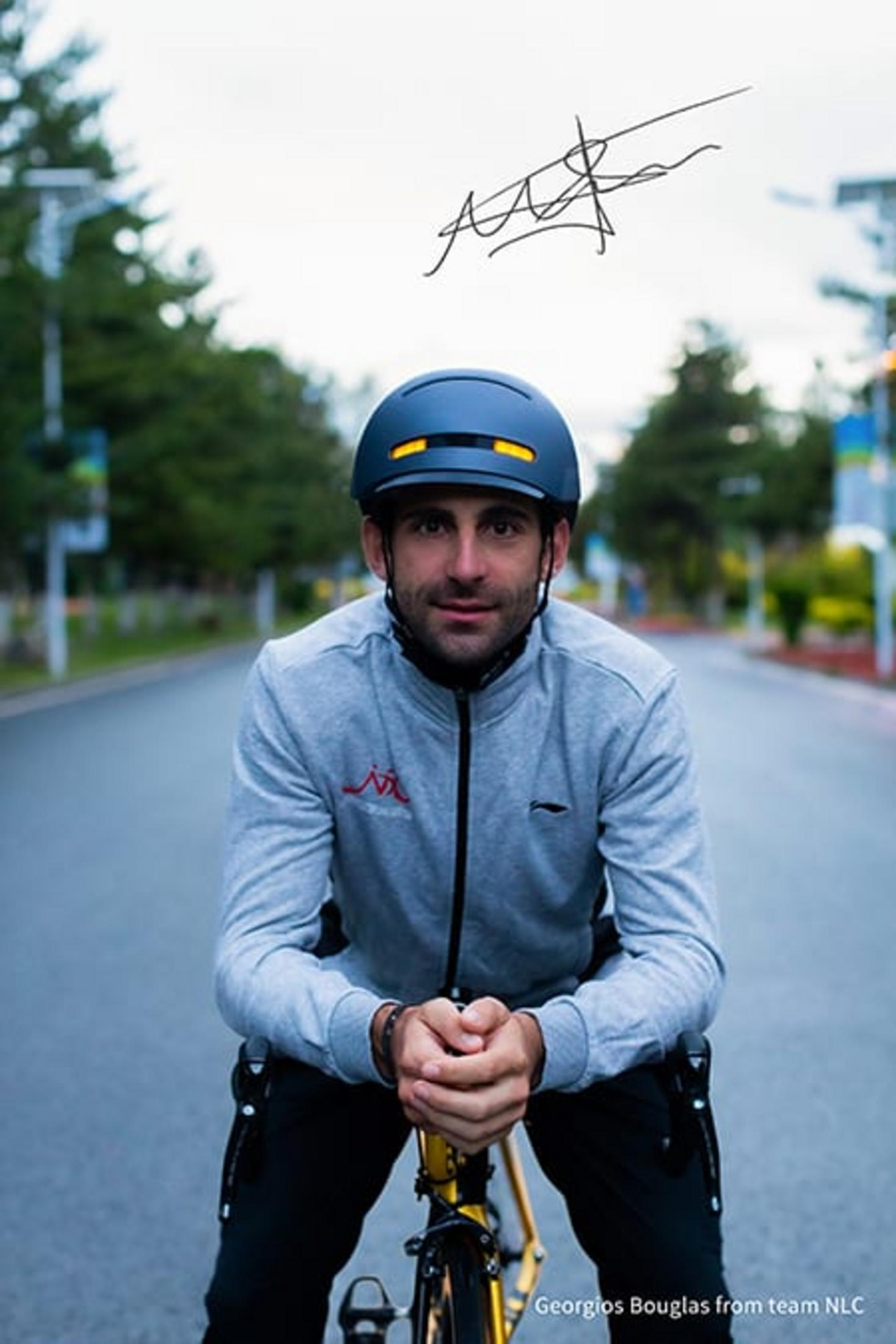 Mann mit Helm auf Fahrrad, grauer Pullover, Straße im Hintergrund.
