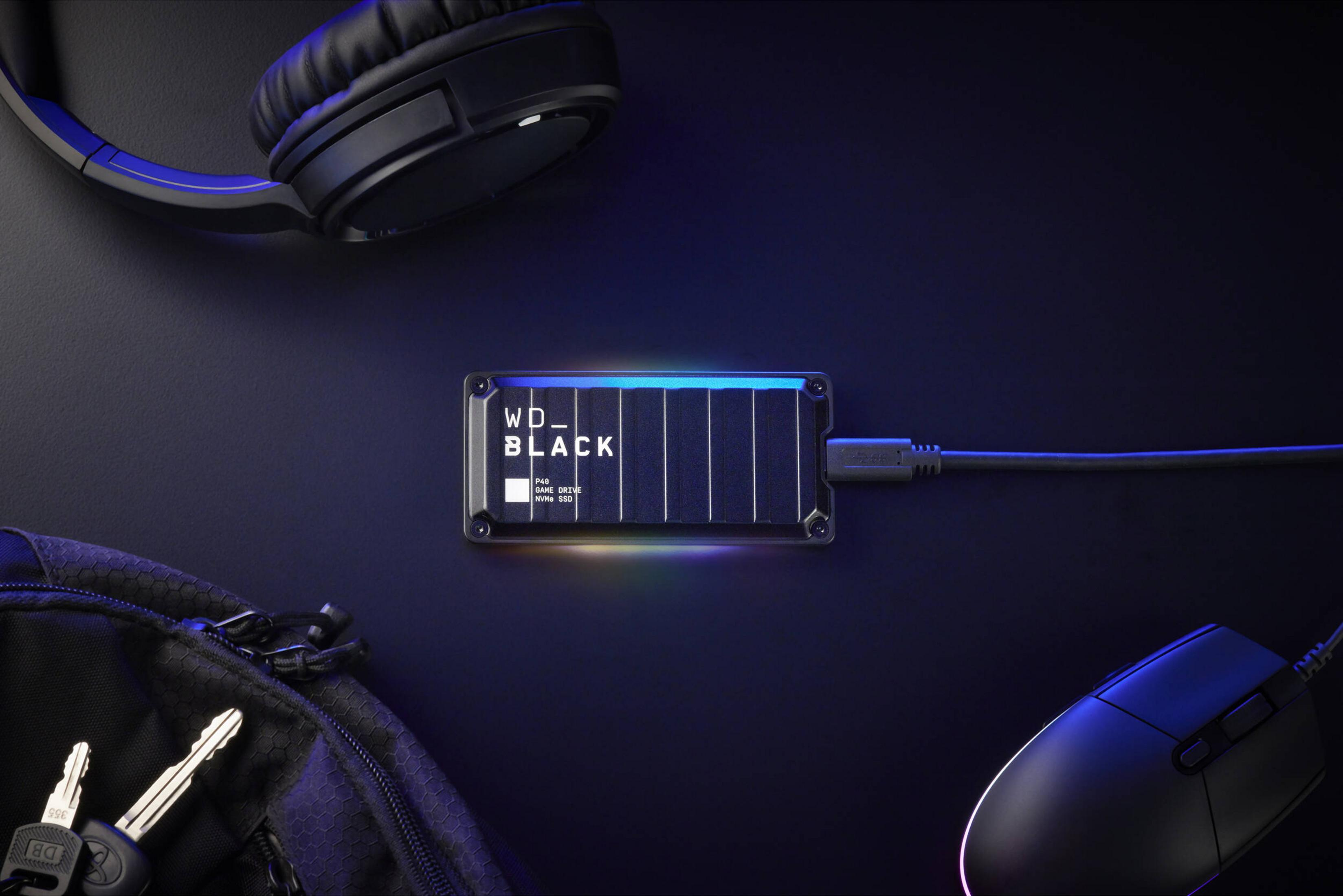 Zewnętrzny dysk SSD WD Black, słuchawki, mysz i klucze na czarnym tle.