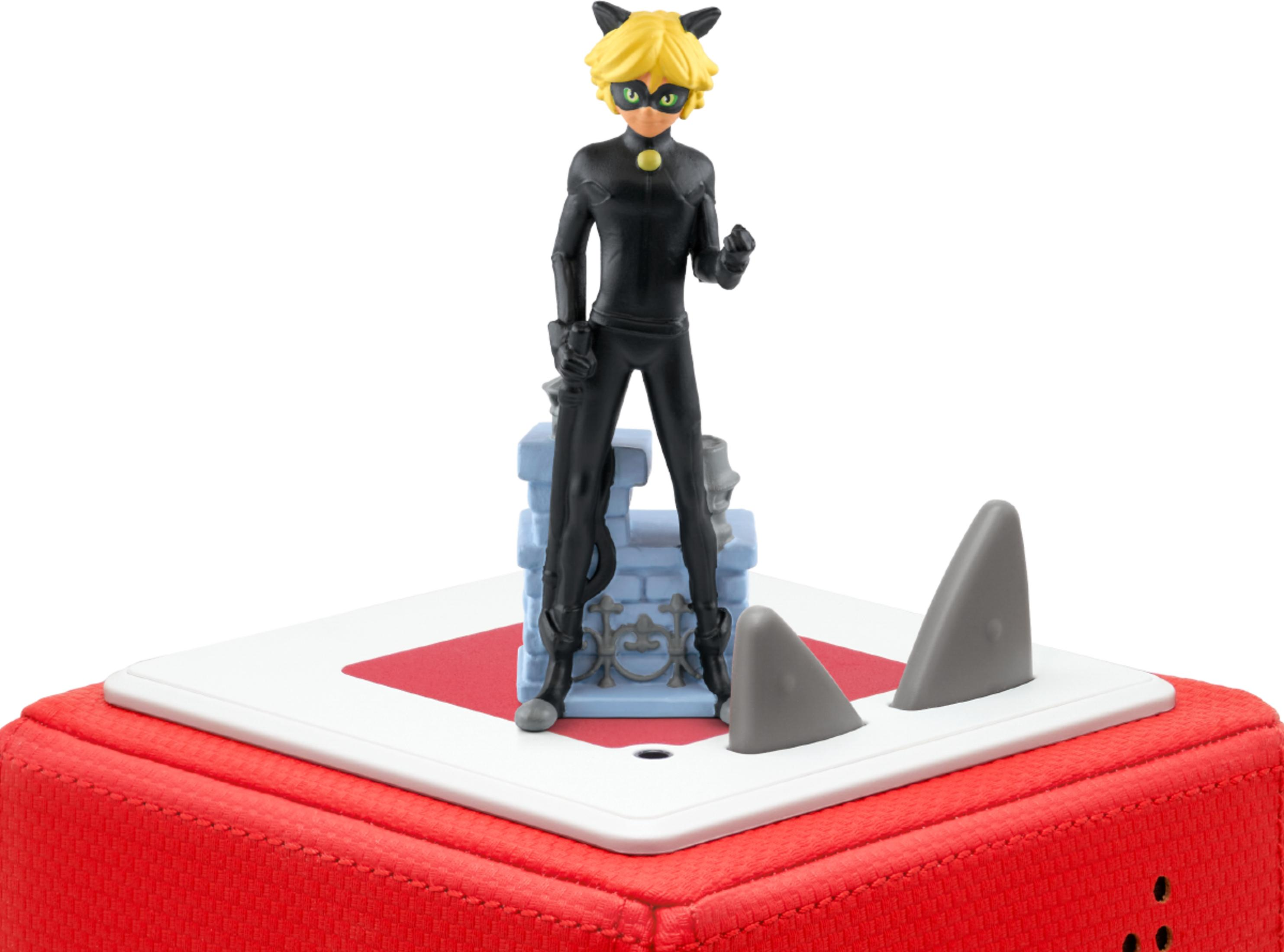 Eine Figur von Cat Noir steht auf einem Spielzeug. Graue Haifischflossen ragen aus der weißen Oberfläche.