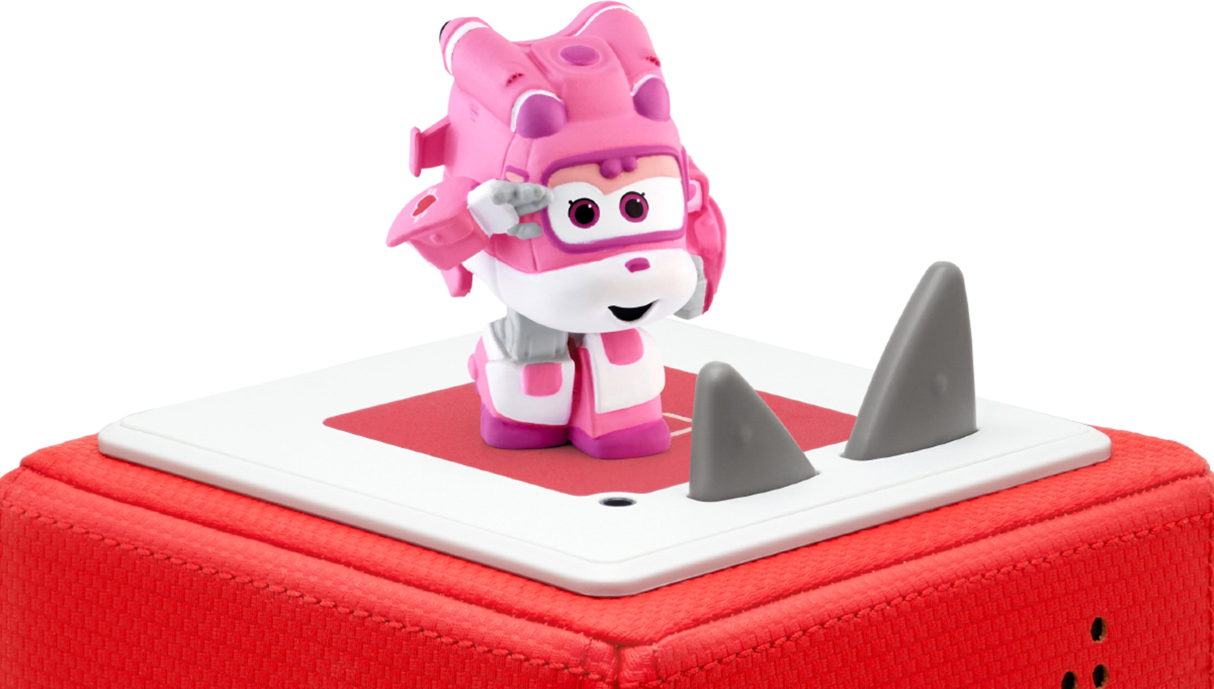 Eine pinke Figur mit Flügeln steht auf einer roten und weißen Plattform mit zwei grauen Haifischflossen.