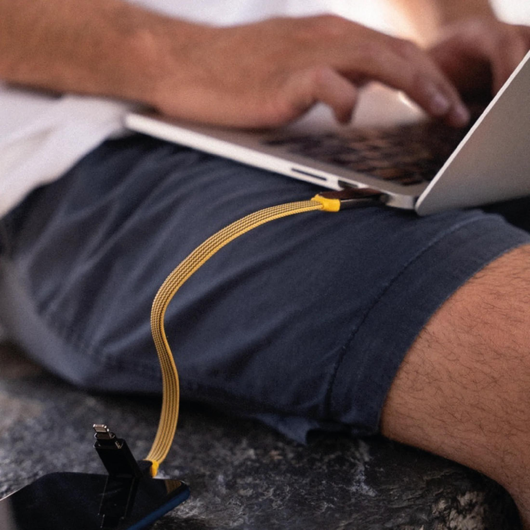 Een man typt op een laptop terwijl een oplaadkabel een smartphone verbindt.