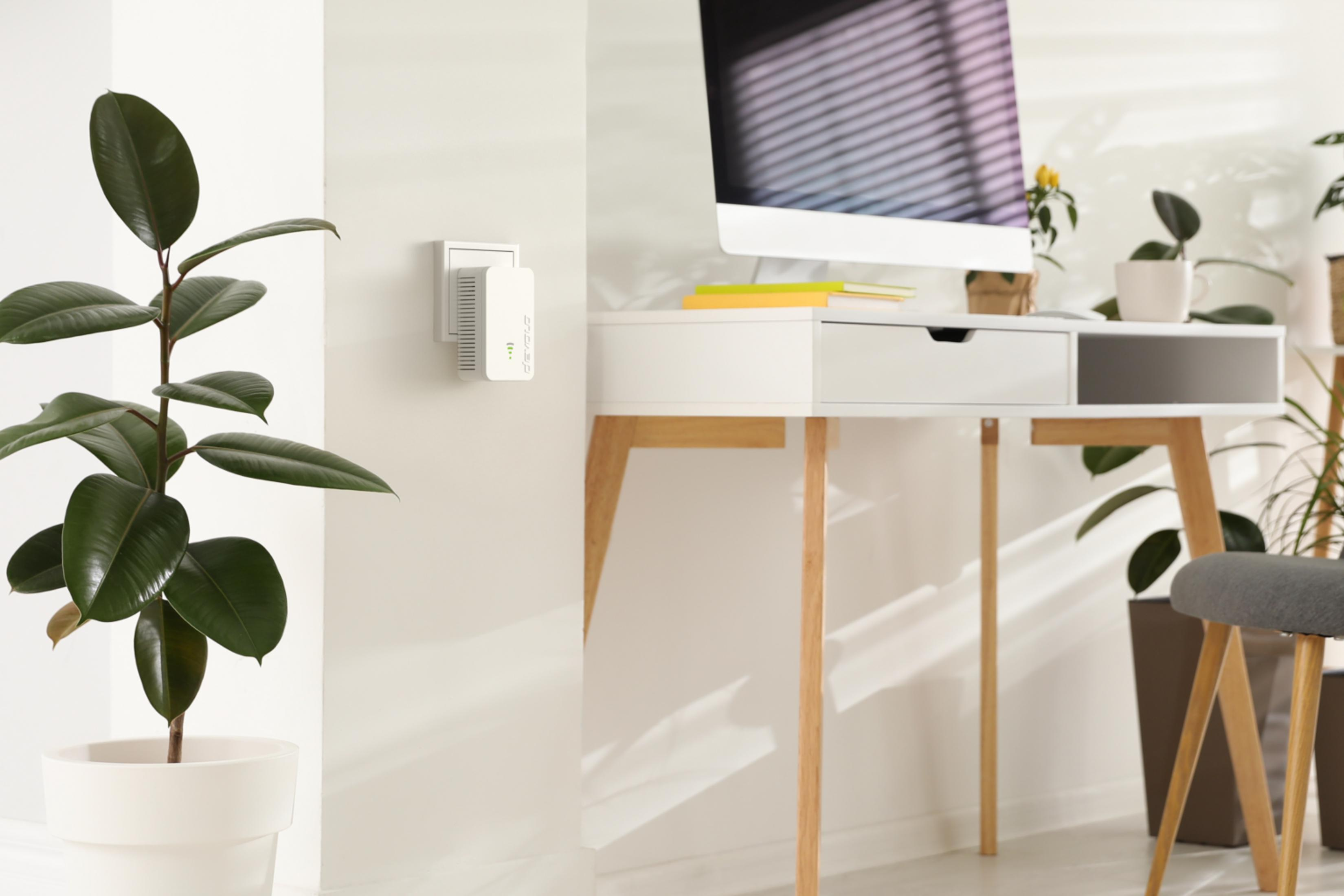 A white WiFi extender is plugged into the wall next to a large potted plant.