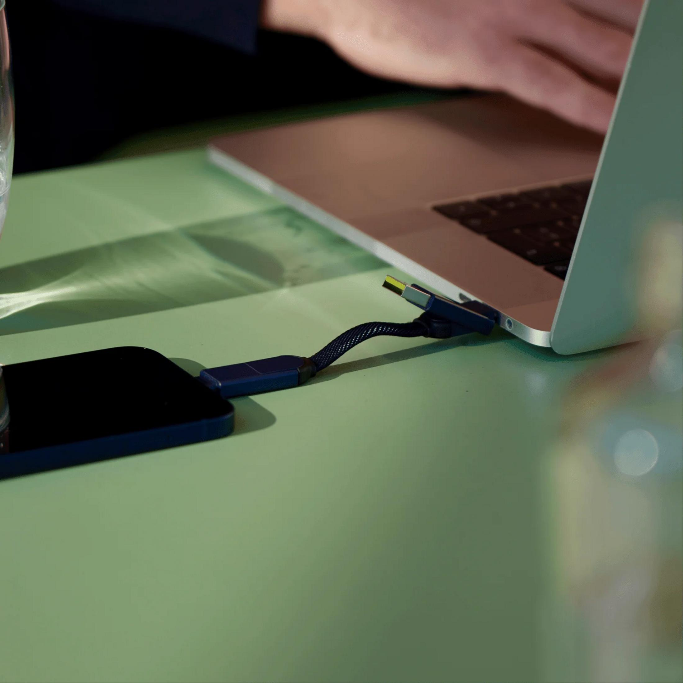 Een man laadt zijn telefoon op met een laptop op een groene tafel.