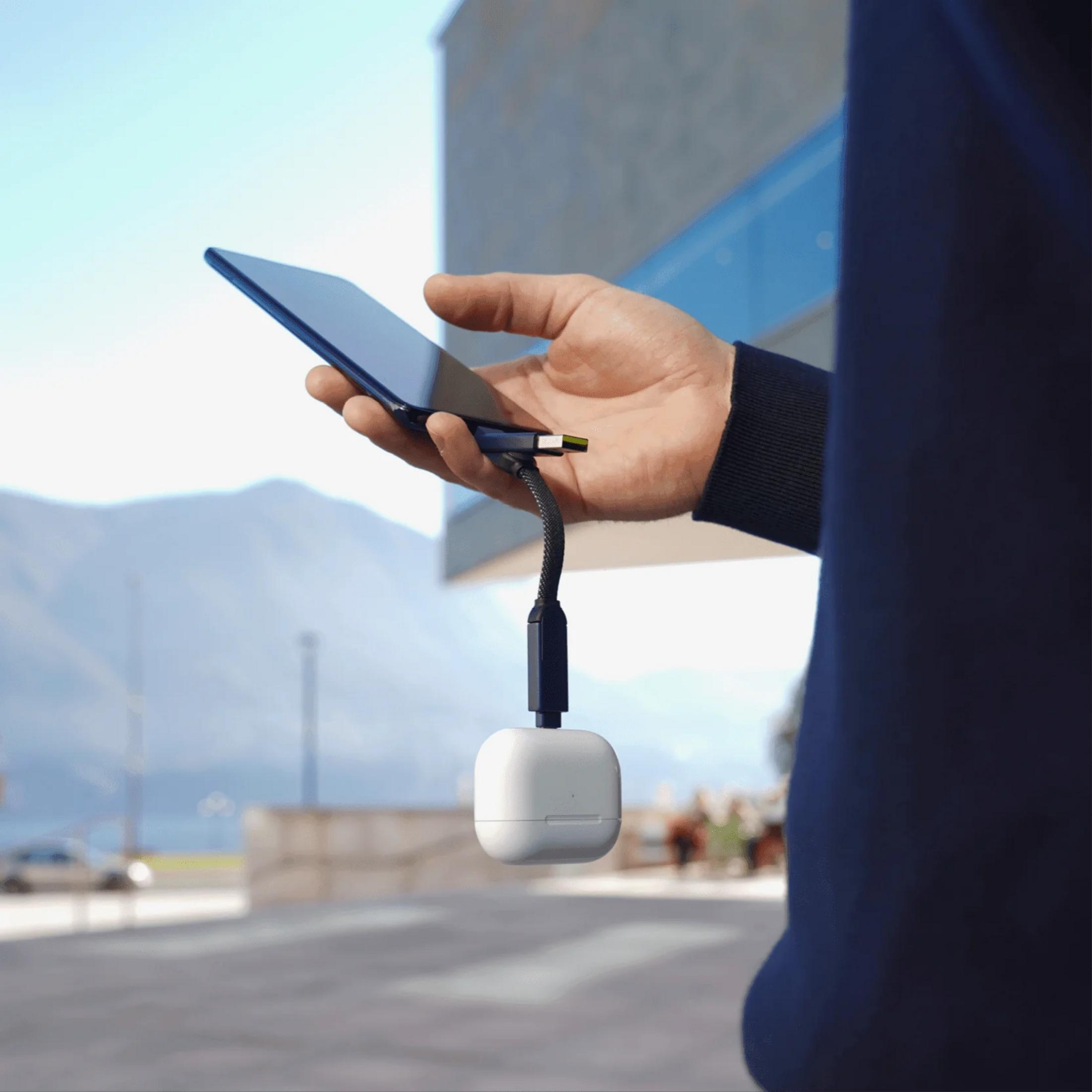 Een hand houdt een blauwe smartphone vast met een oplaadkabel en witte oplaadcase eraan.