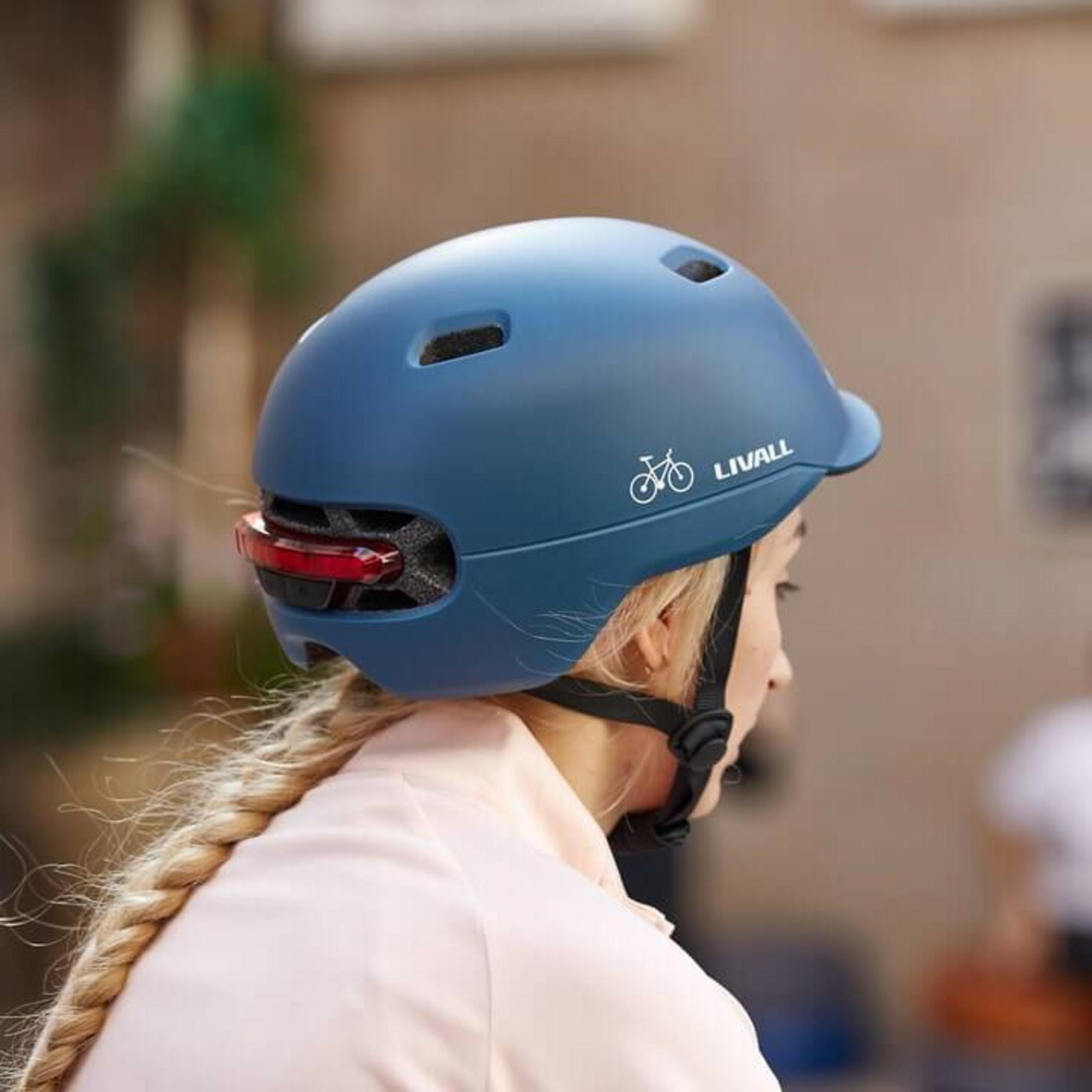 Una donna con casco da bici blu, fanale posteriore e treccia.