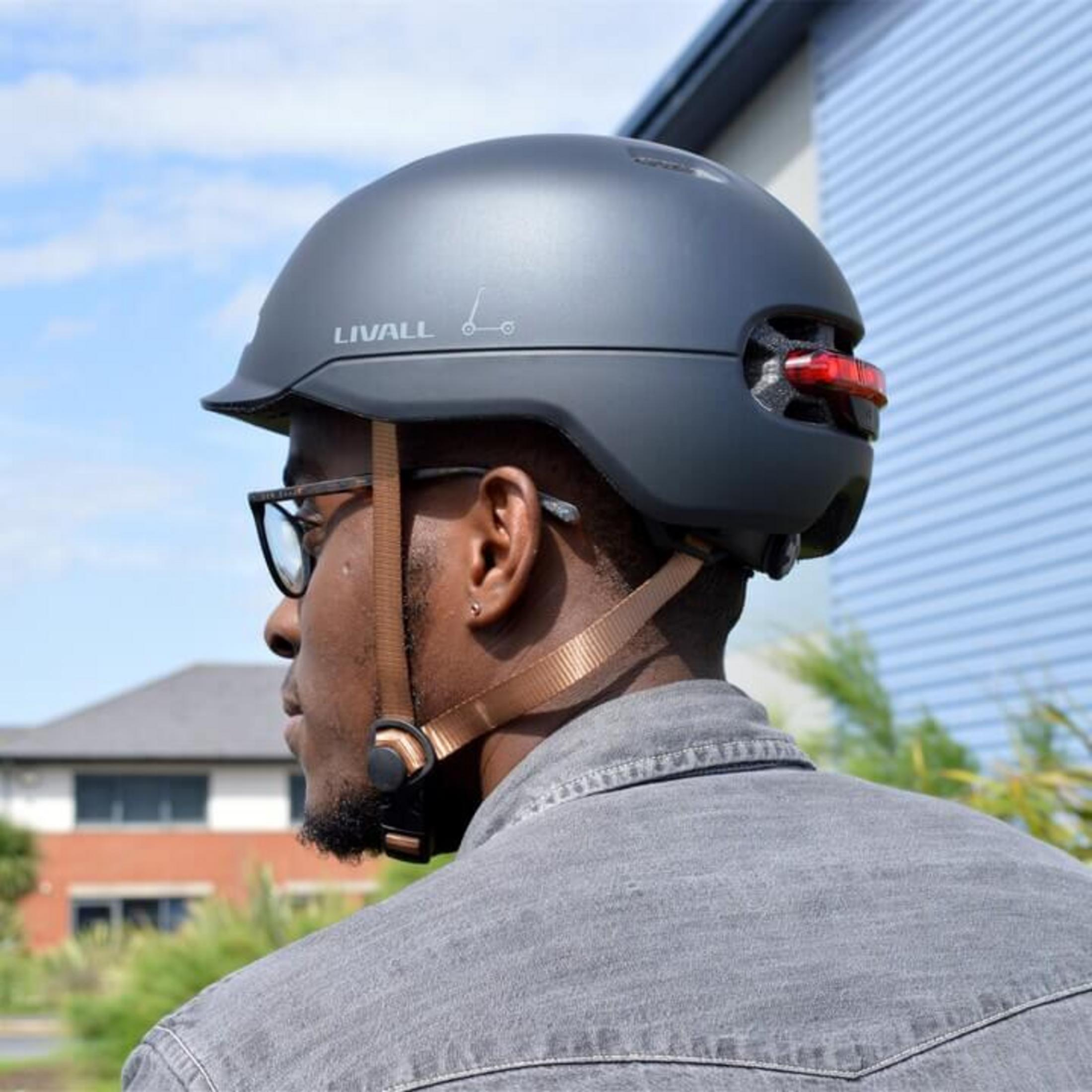 Uomo con casco grigio e luce posteriore rossa, indossa occhiali.