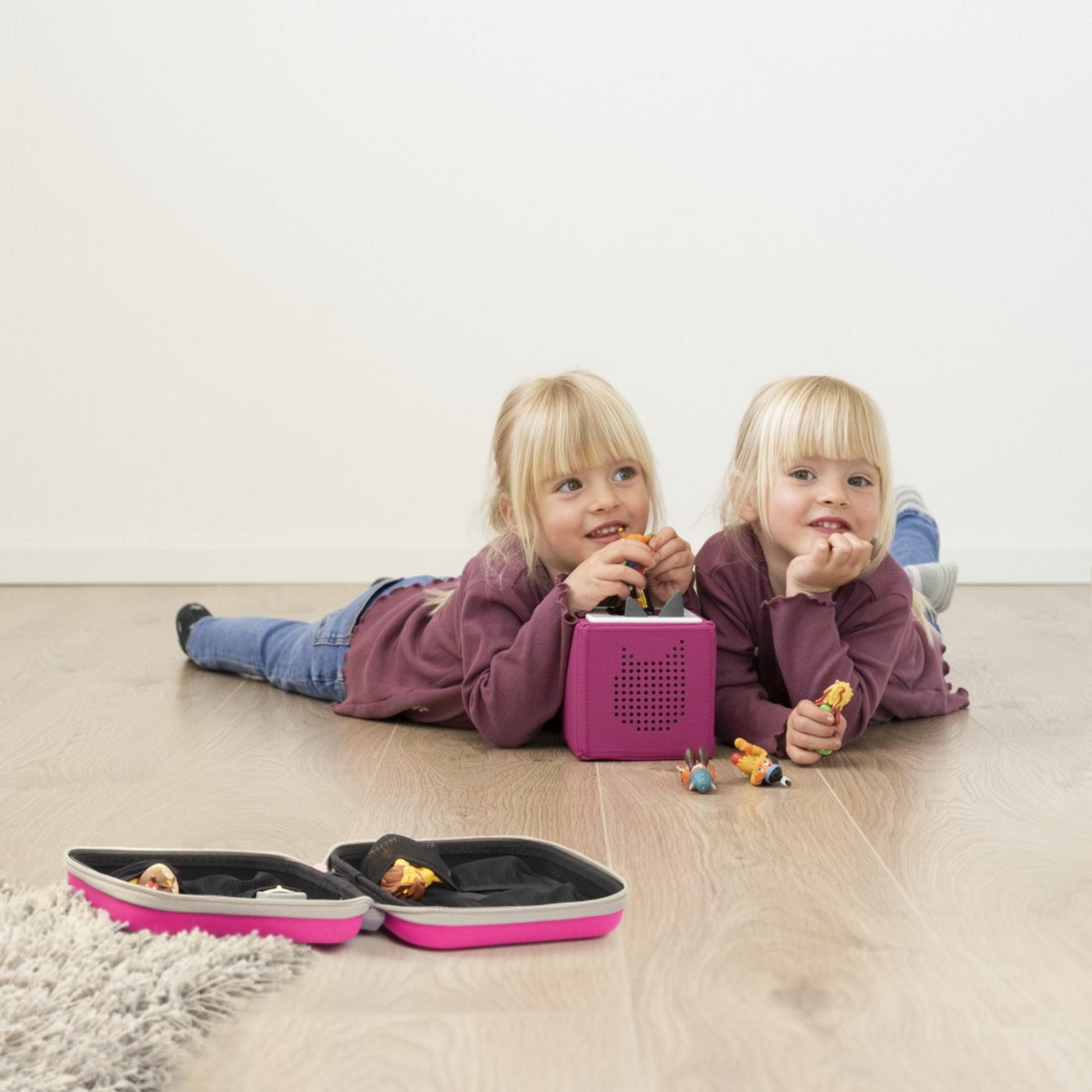 Zwei blonde Mädchen liegen auf dem Boden und spielen mit kleinen Figuren und einem pinken Würfel.