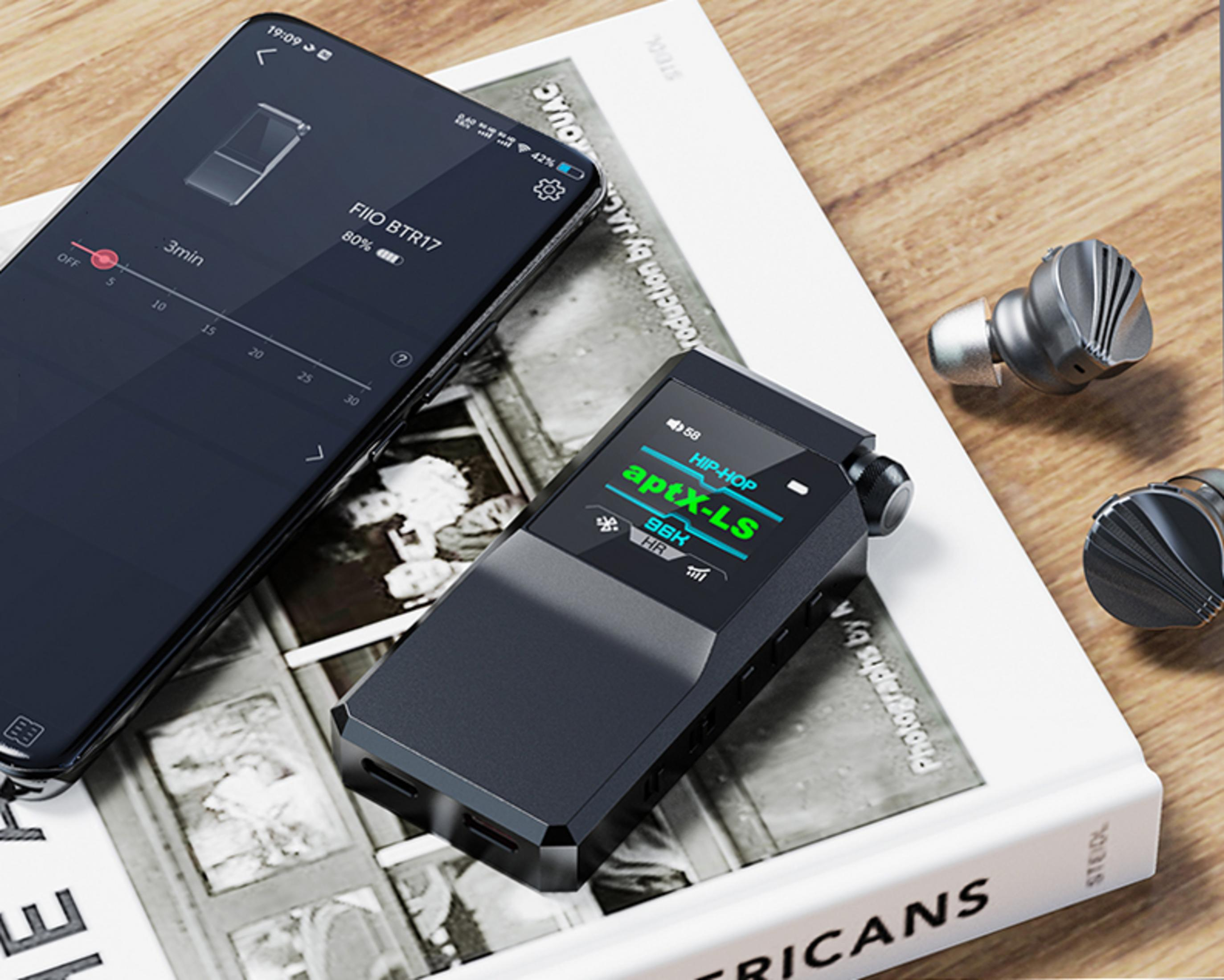 Un smartphone, un reproductor de audio y auriculares descansan sobre un libro.