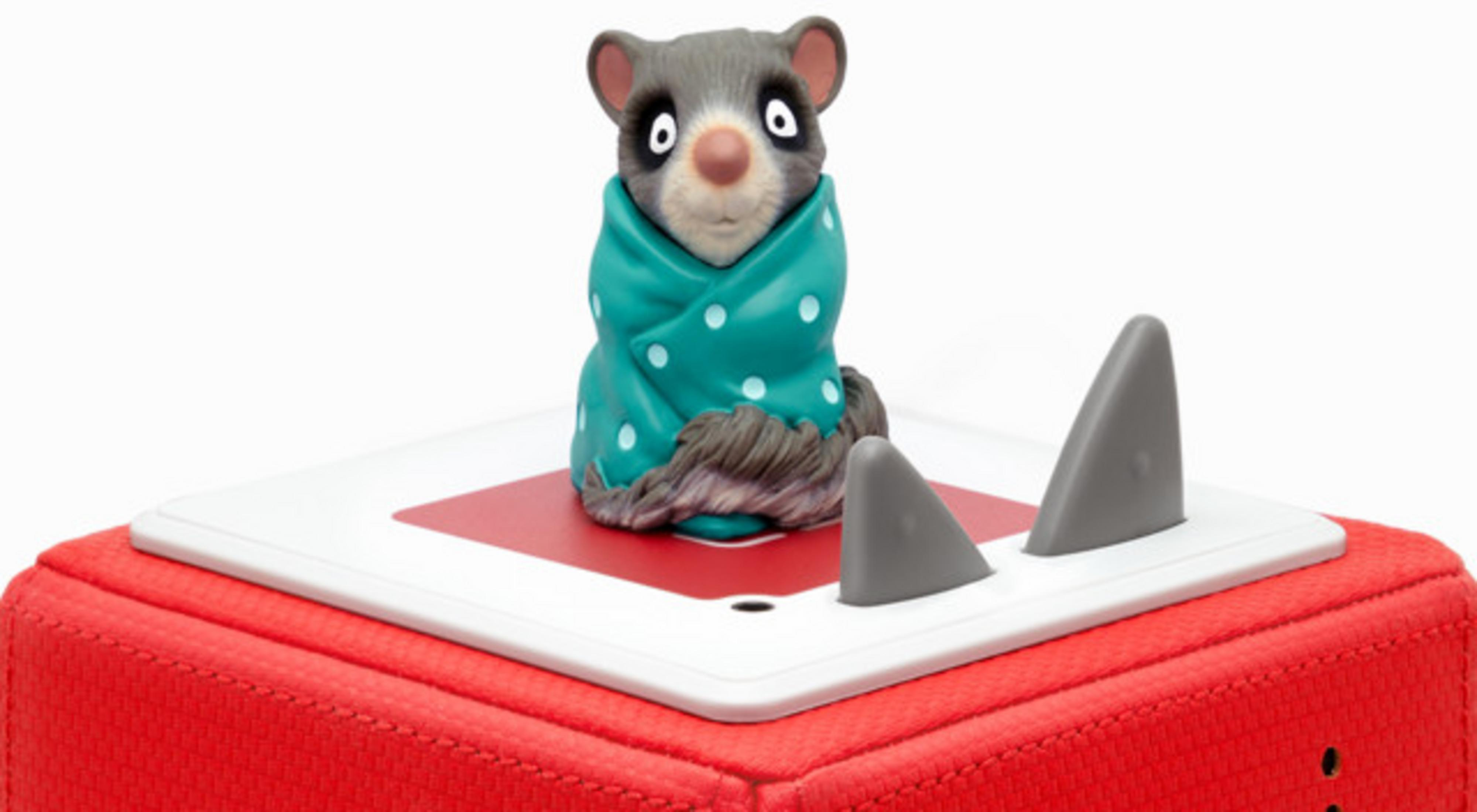 Ein Spielzeug-Opossum in einer türkisen Decke mit Tupfen auf einem roten Würfel.