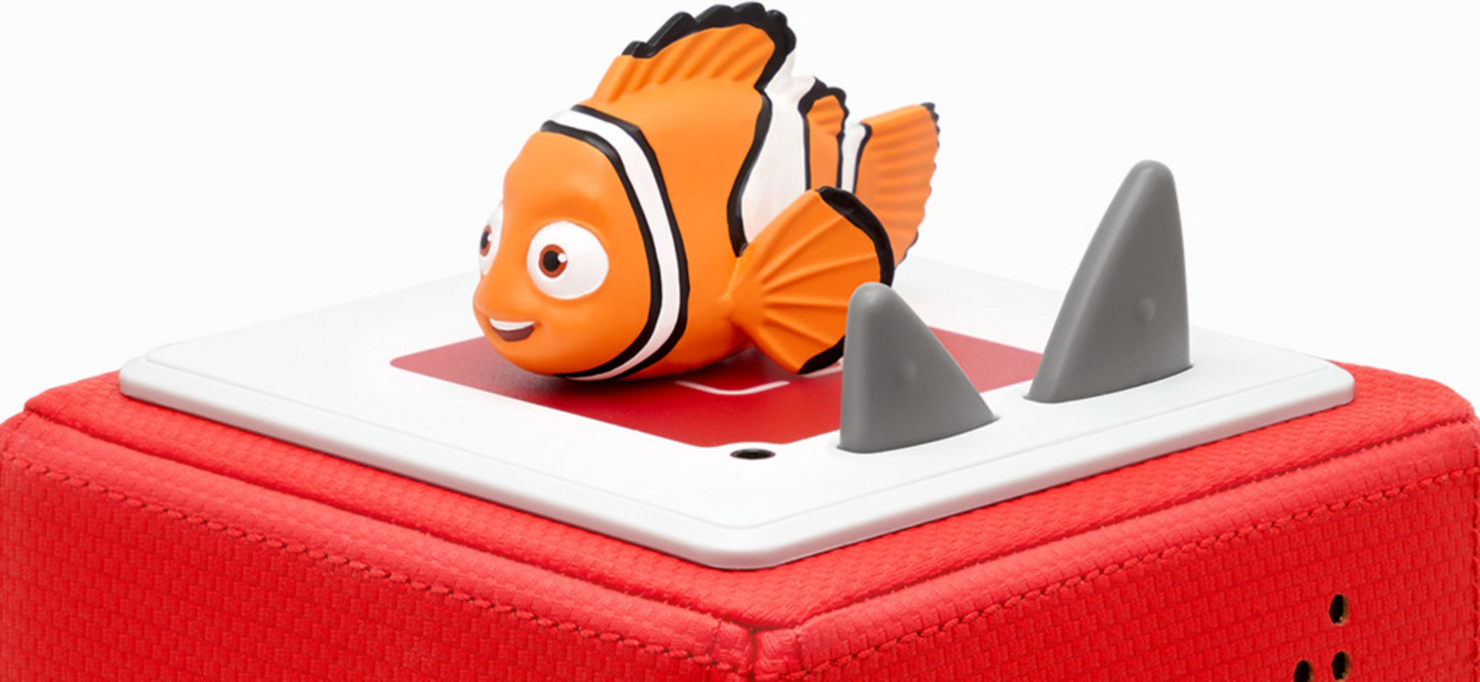 Un pesce pagliaccio arancione e bianco su un cubo rosso con pinne di squalo grigie.