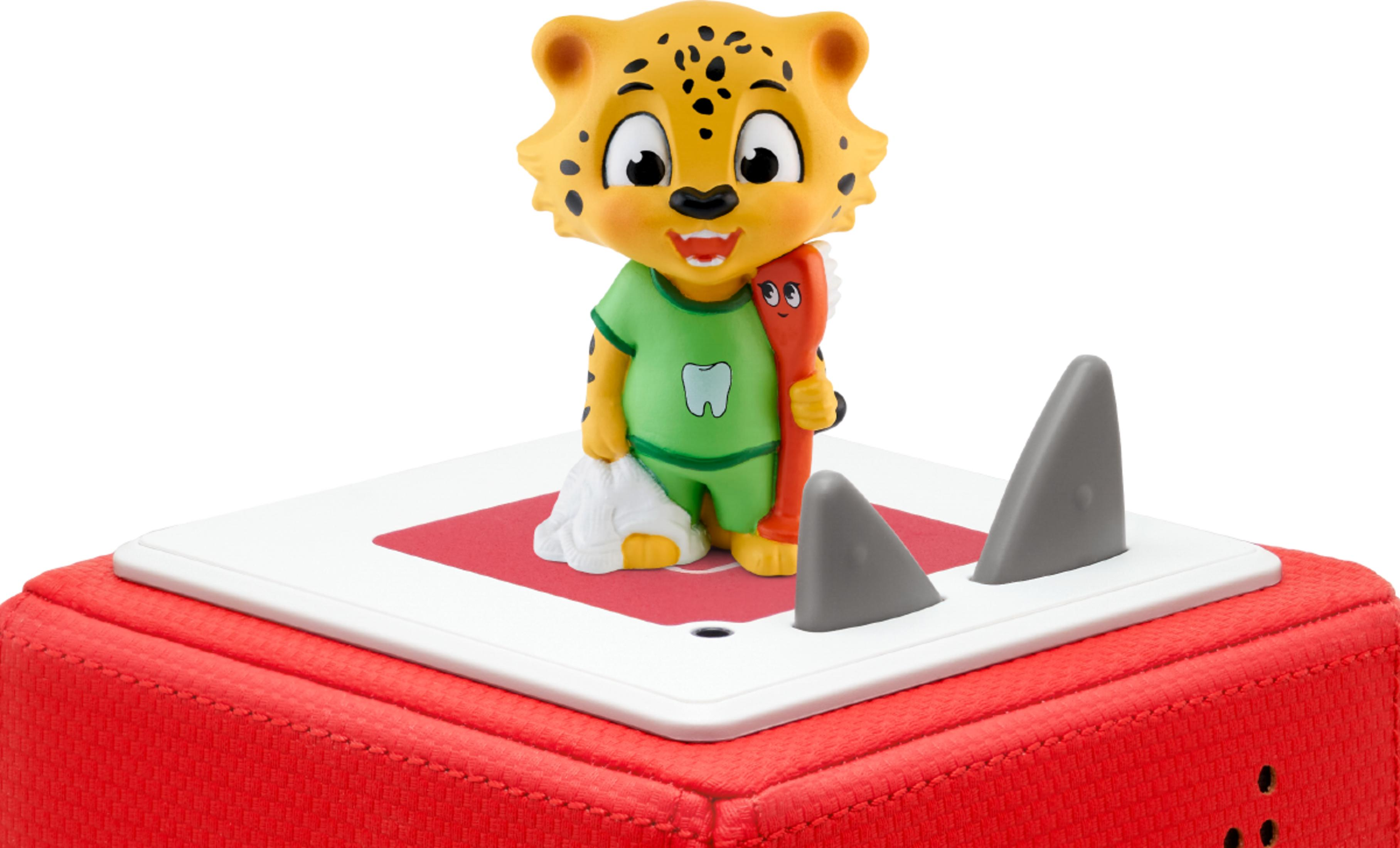 Ein Leopard-Spielzeug steht auf einem roten Würfel mit Hai-Flossen und einer Zahnbürste.