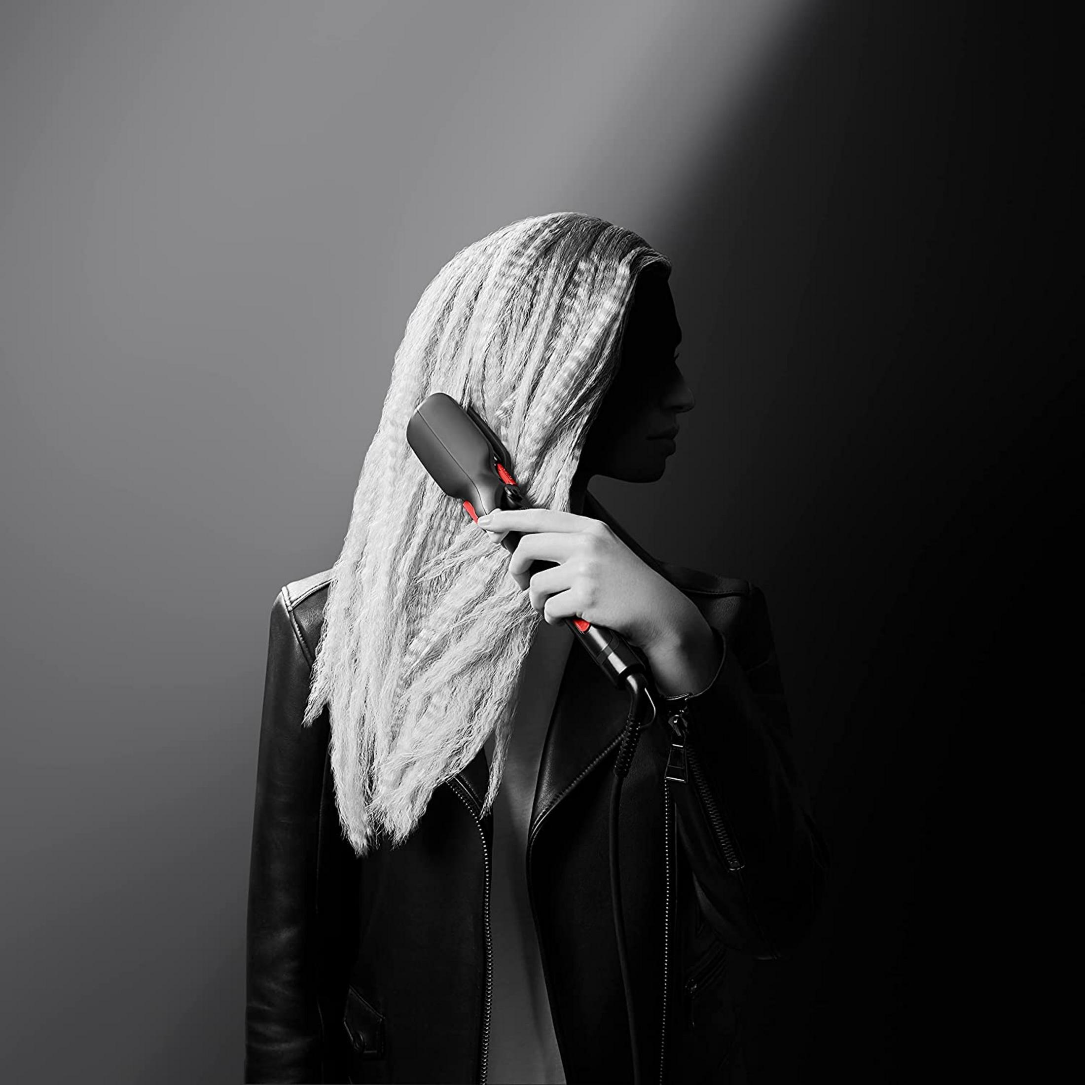 Kobieta z długimi, jasnymi włosami używa lokówki z czerwonymi akcentami.