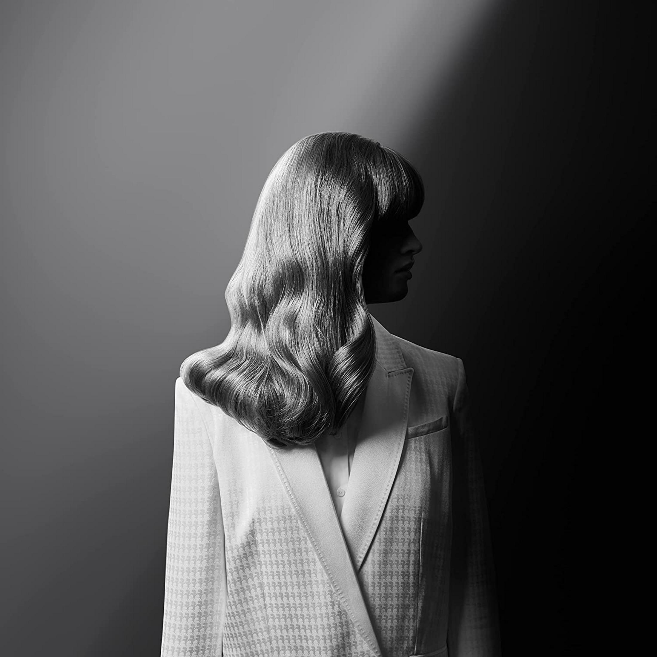 Kobieta z falowanymi włosami w garniturze we wzory na ciemnym tle.