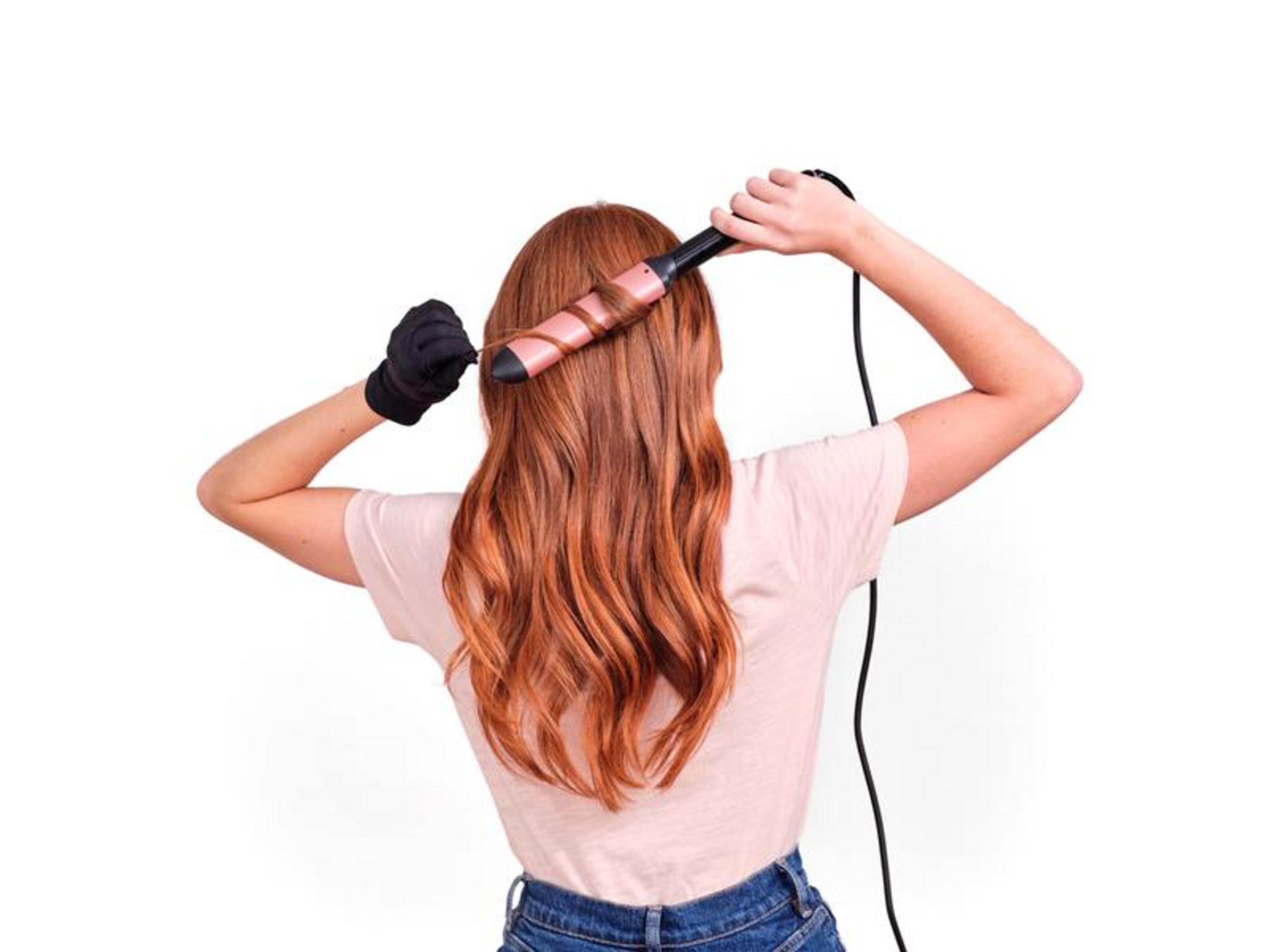 Eine Frau mit roten Haaren lockt ihr Haar mit einem rosa Lockenstab.