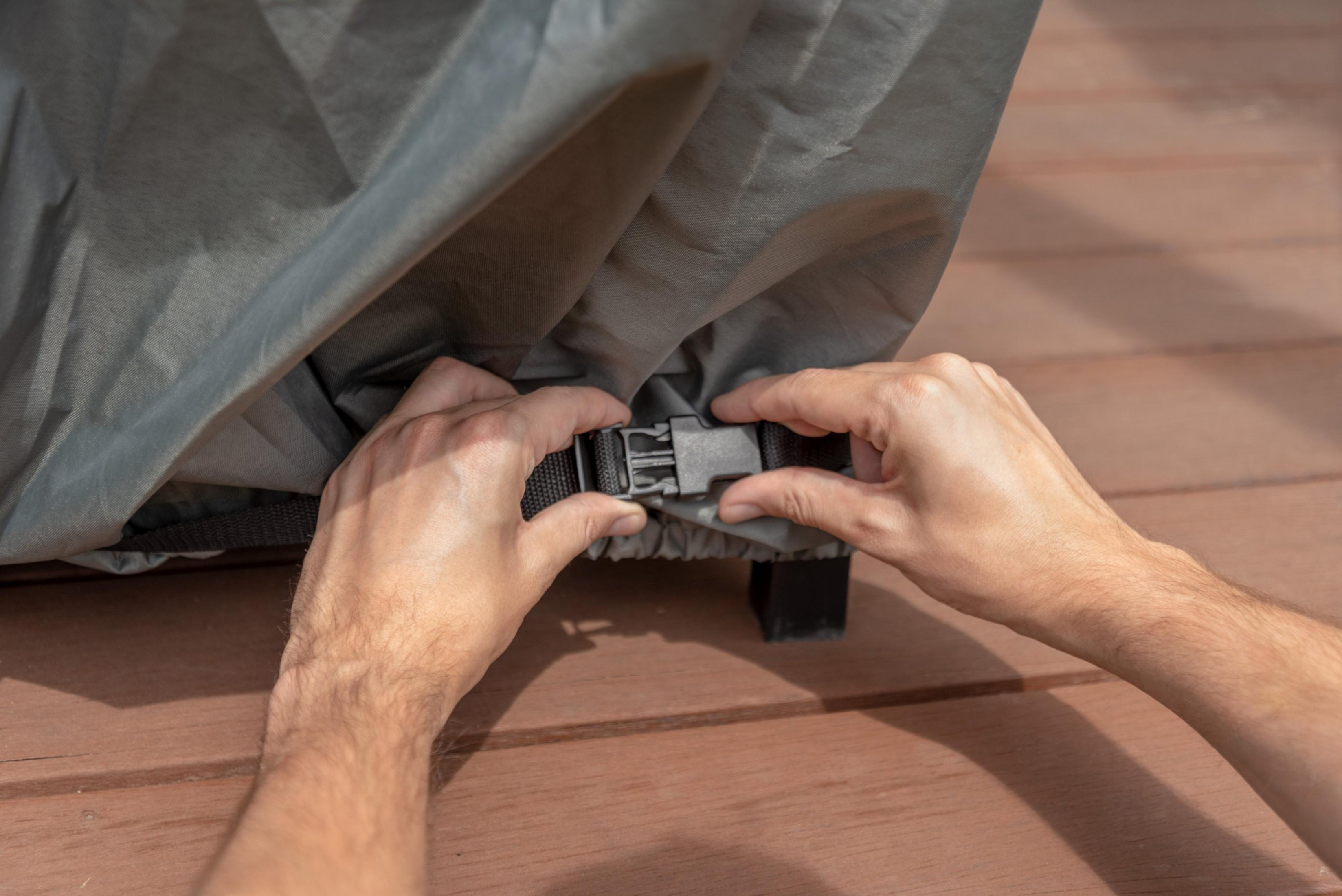 Mains attachant une boucle de couverture grise sur une terrasse en bois.