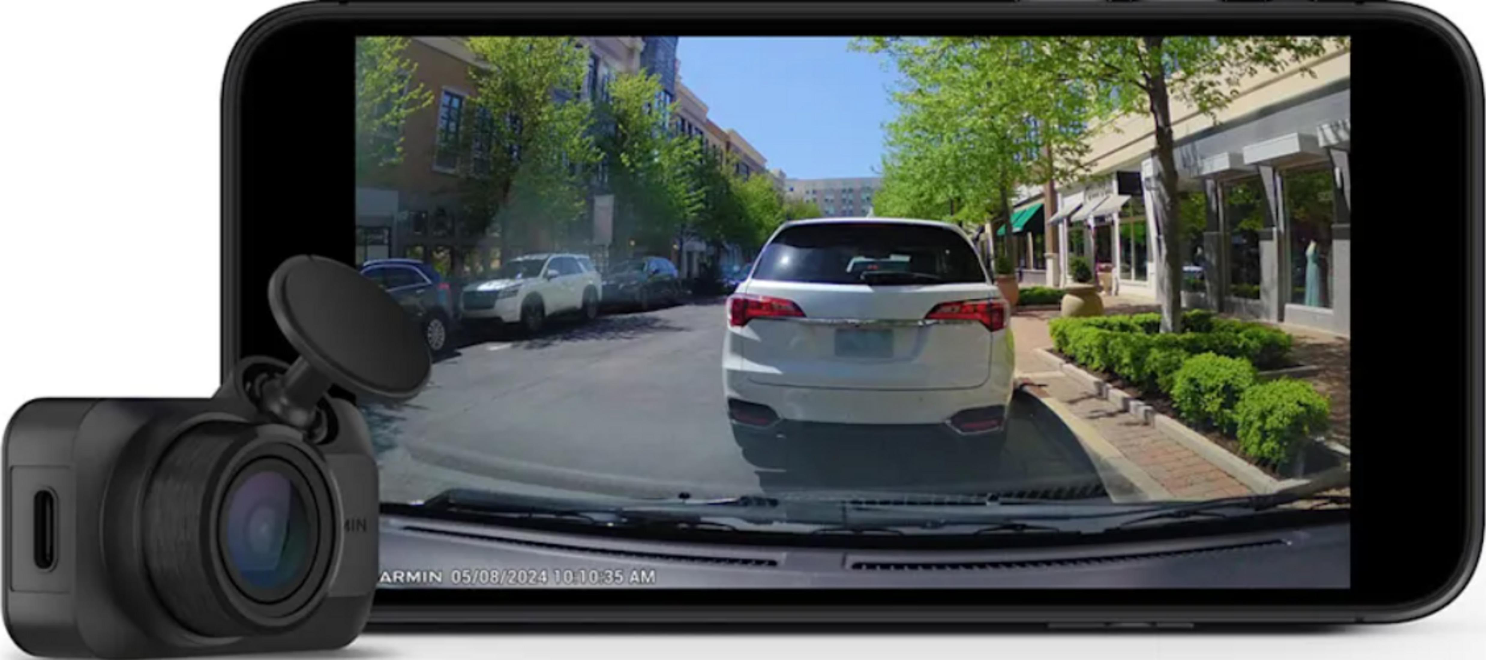 Ein schwarzer Dashcam-Recorder vor einem Smartphone mit Blick auf eine Straße mit Autos und Geschäften.