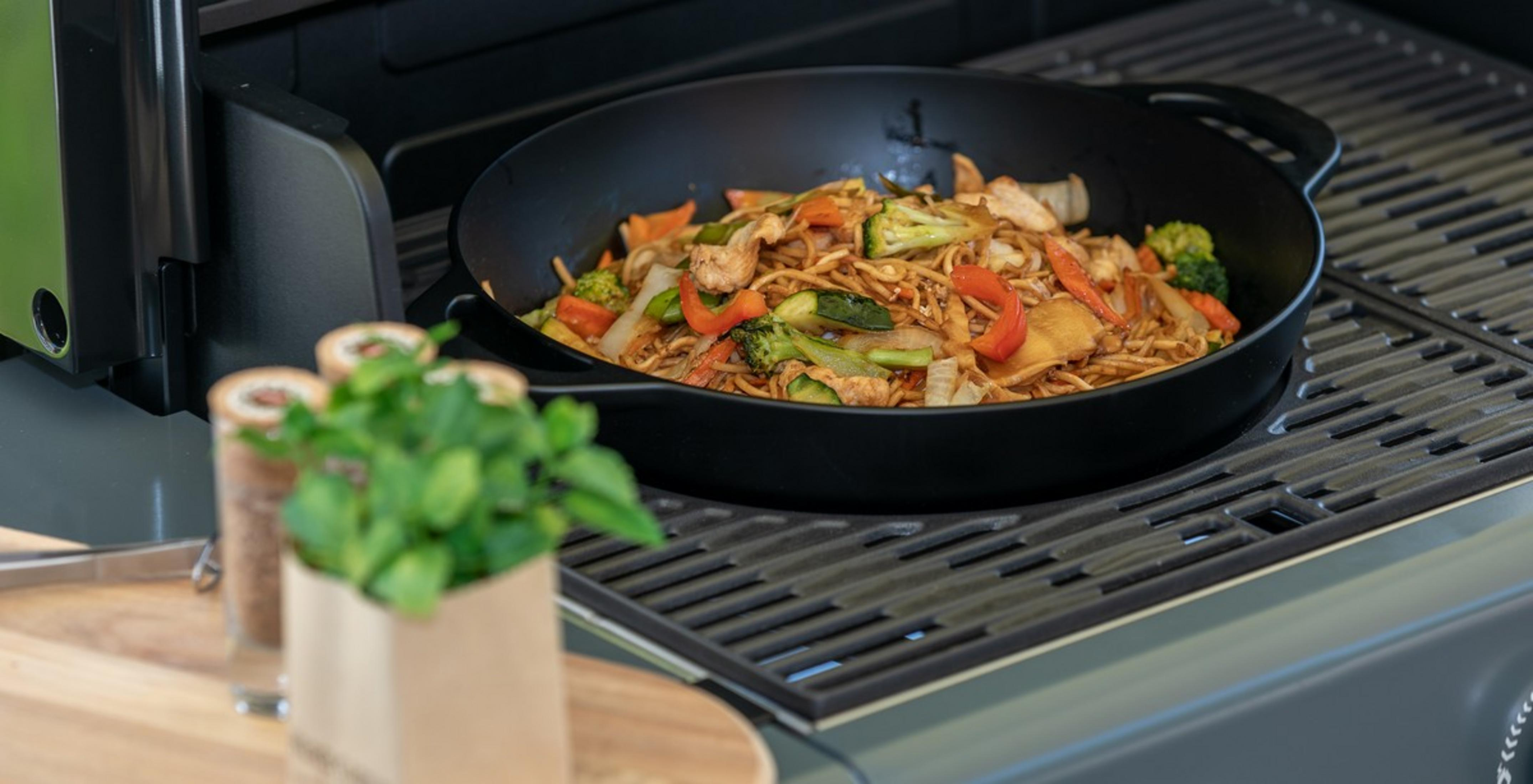 Un wok con fideos, pollo y verduras en una parrilla.