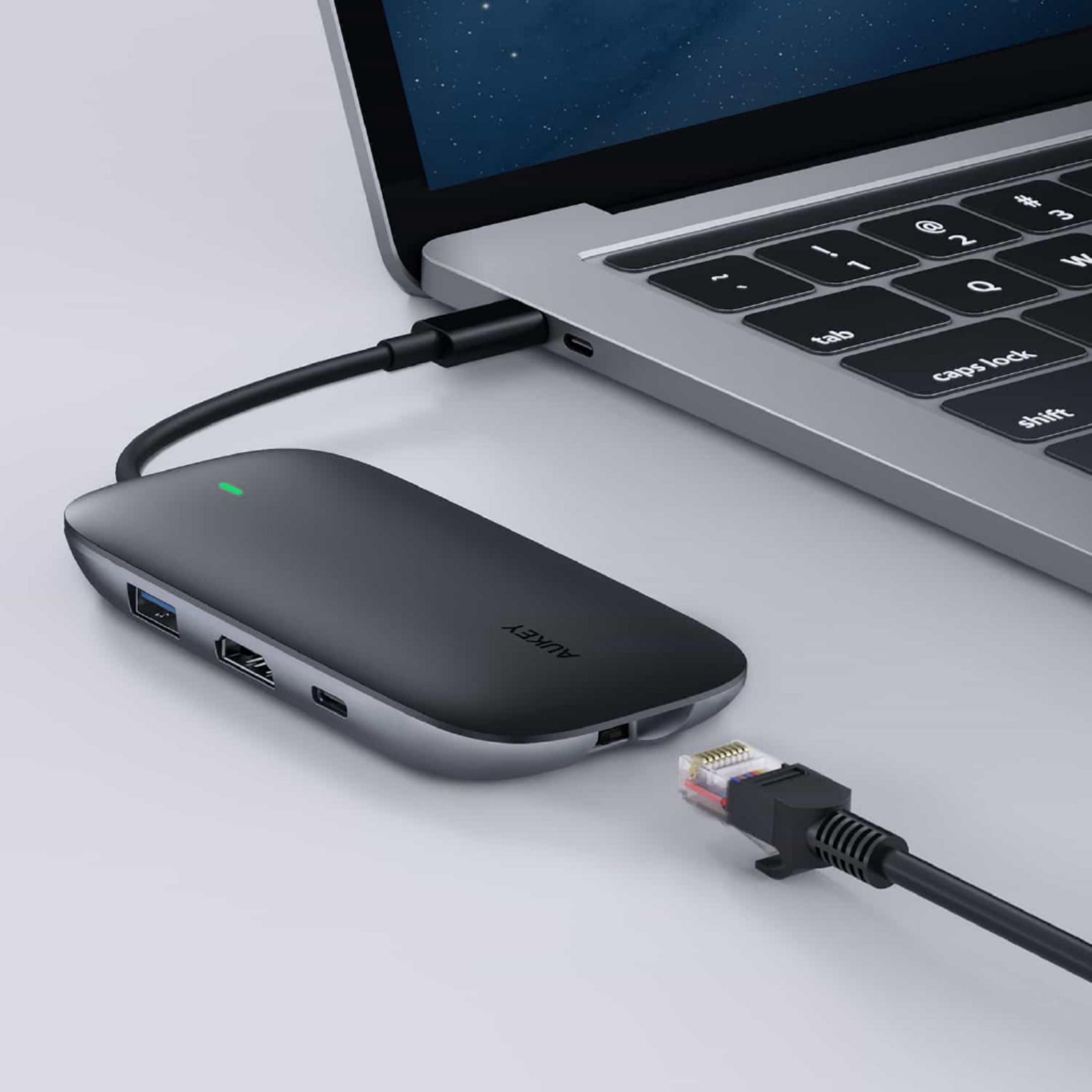 Ein grauer USB-C-Hub ist an ein silbernes Laptop angeschlossen. Ein Netzwerkkabel steckt daneben.