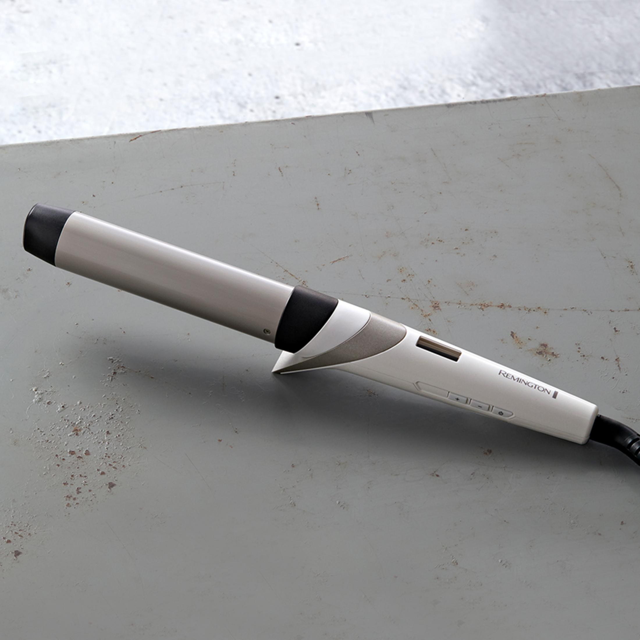 Un ferro arricciacapelli Remington con manico bianco e corpo argentato giace su una superficie grigia.
