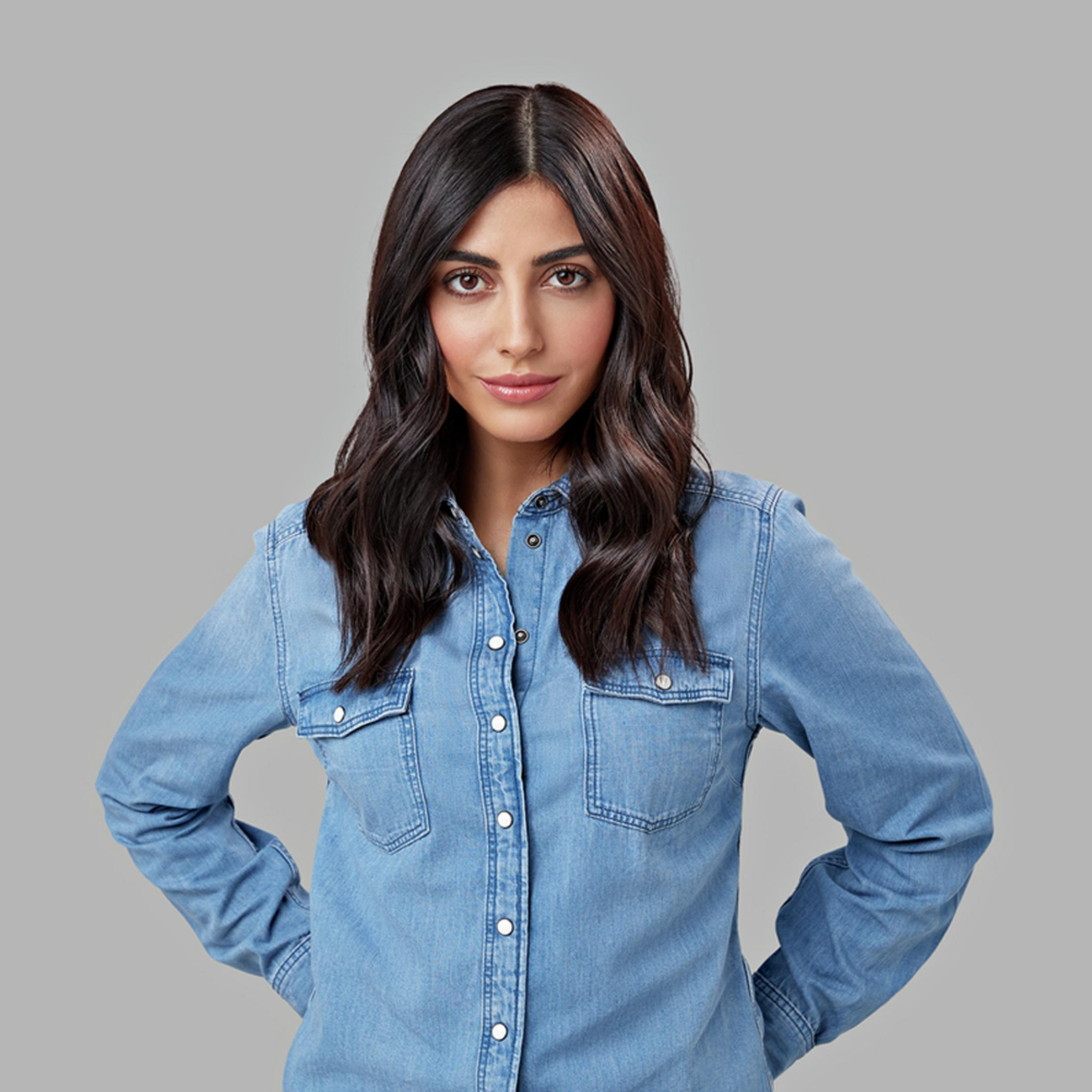 Una donna con i capelli scuri indossa una camicia di jeans blu e guarda la telecamera.