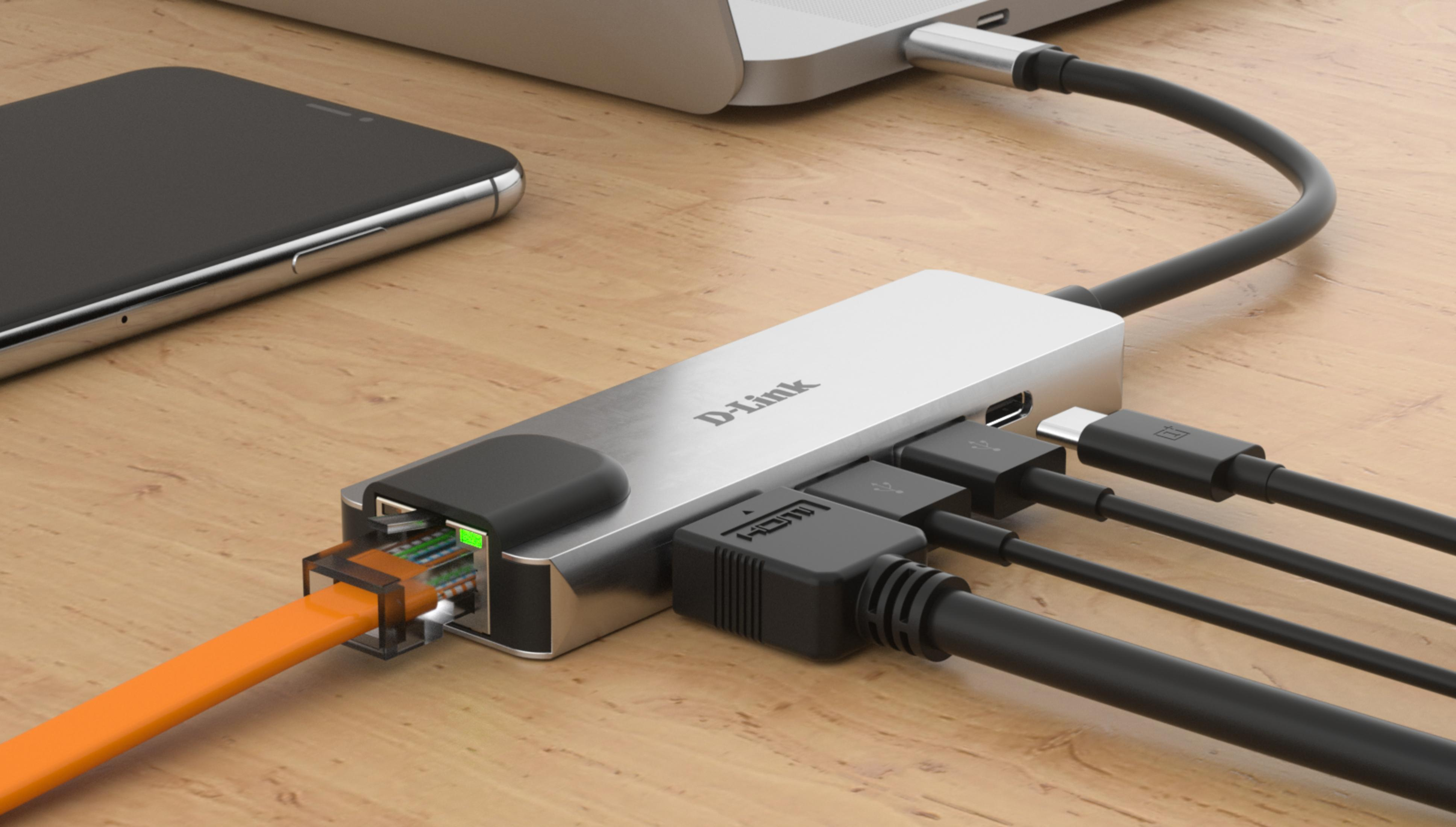 Un hub D-Link collegato a cavi Ethernet, HDMI e USB su una scrivania di legno.