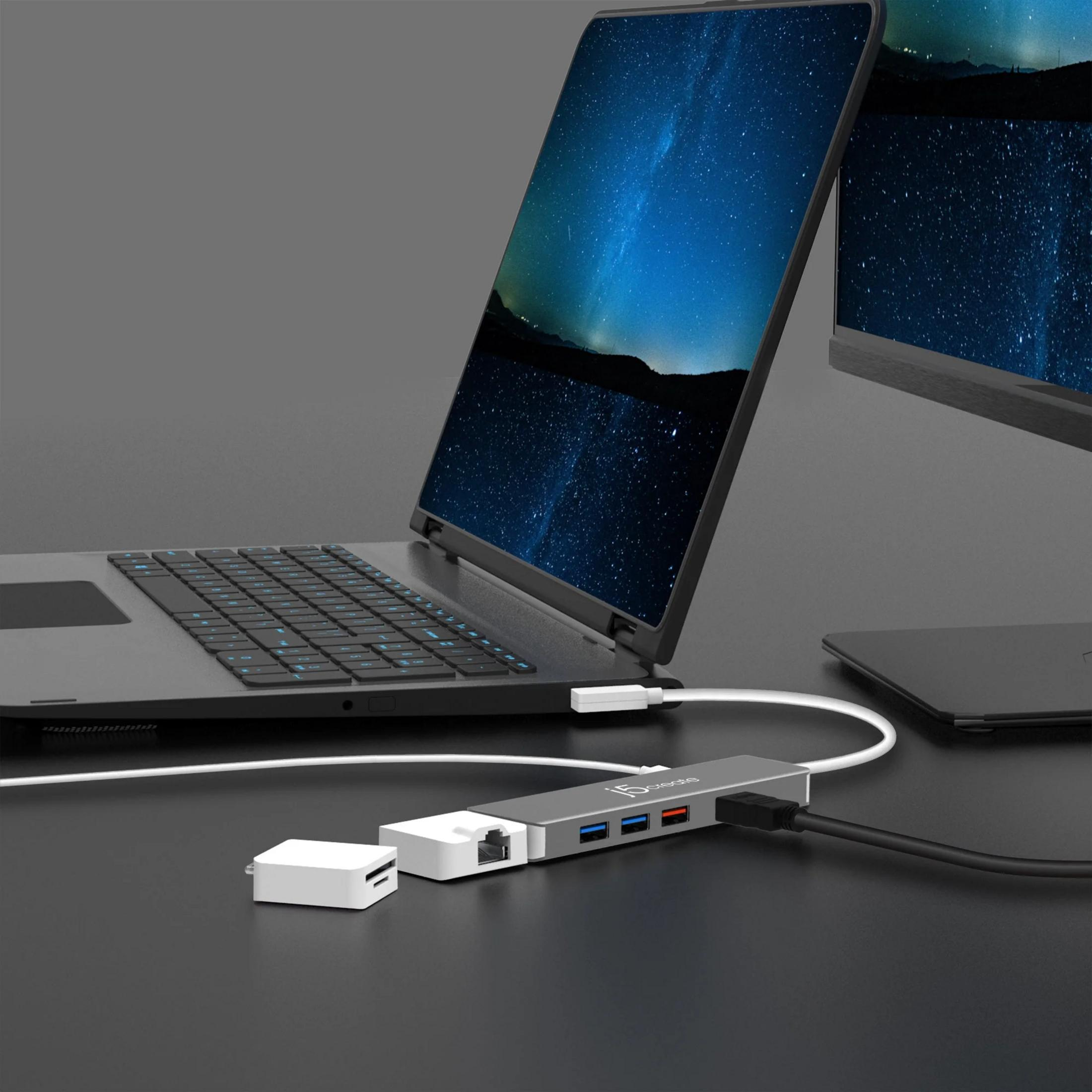 Ein Laptop mit Sternenhimmel-Hintergrund, verbunden mit einem grauen USB-Hub mit SD-Kartenleser.