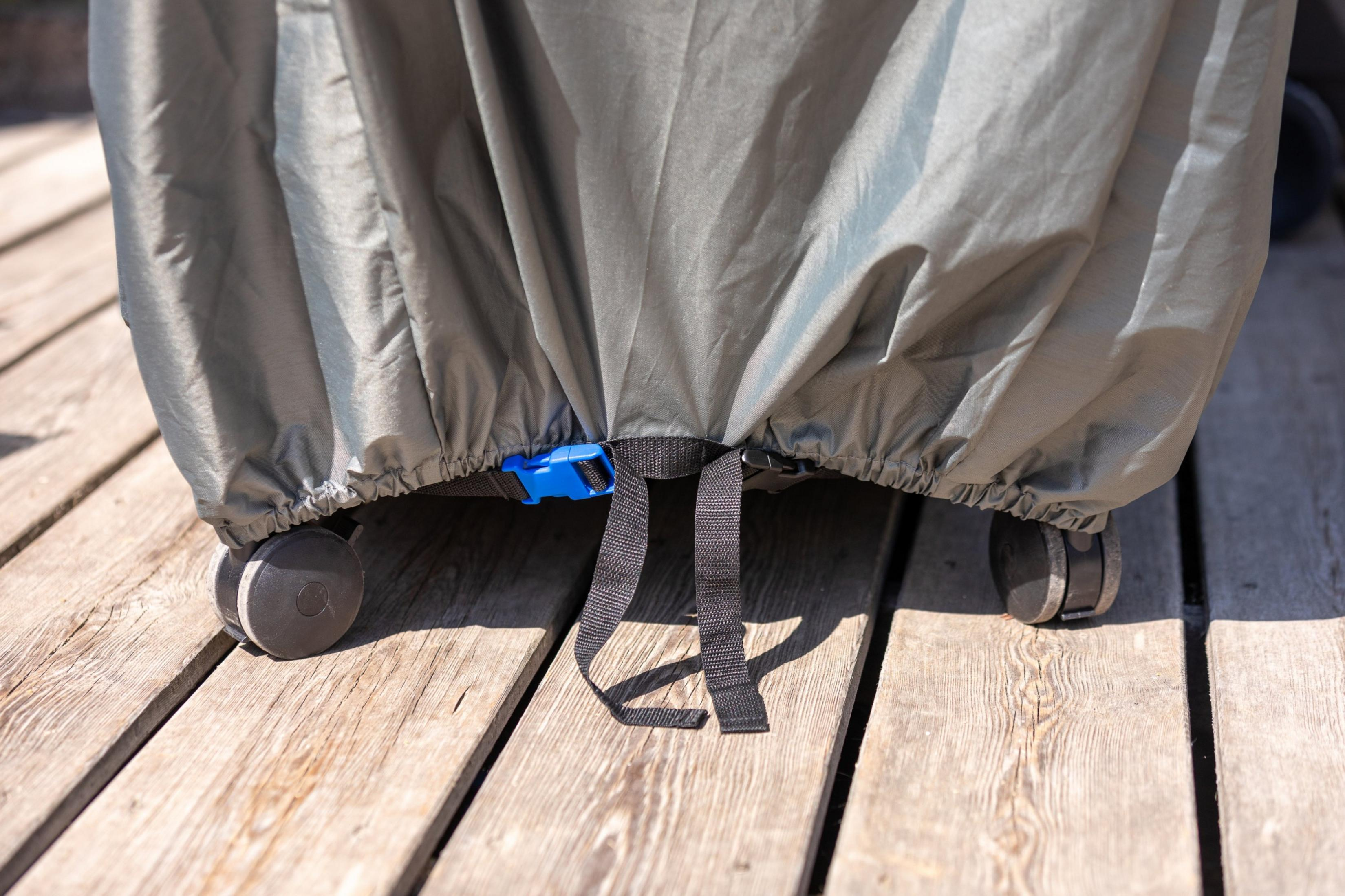 Szara osłona z kołami i niebieskim klipsem na drewnianych deskach.