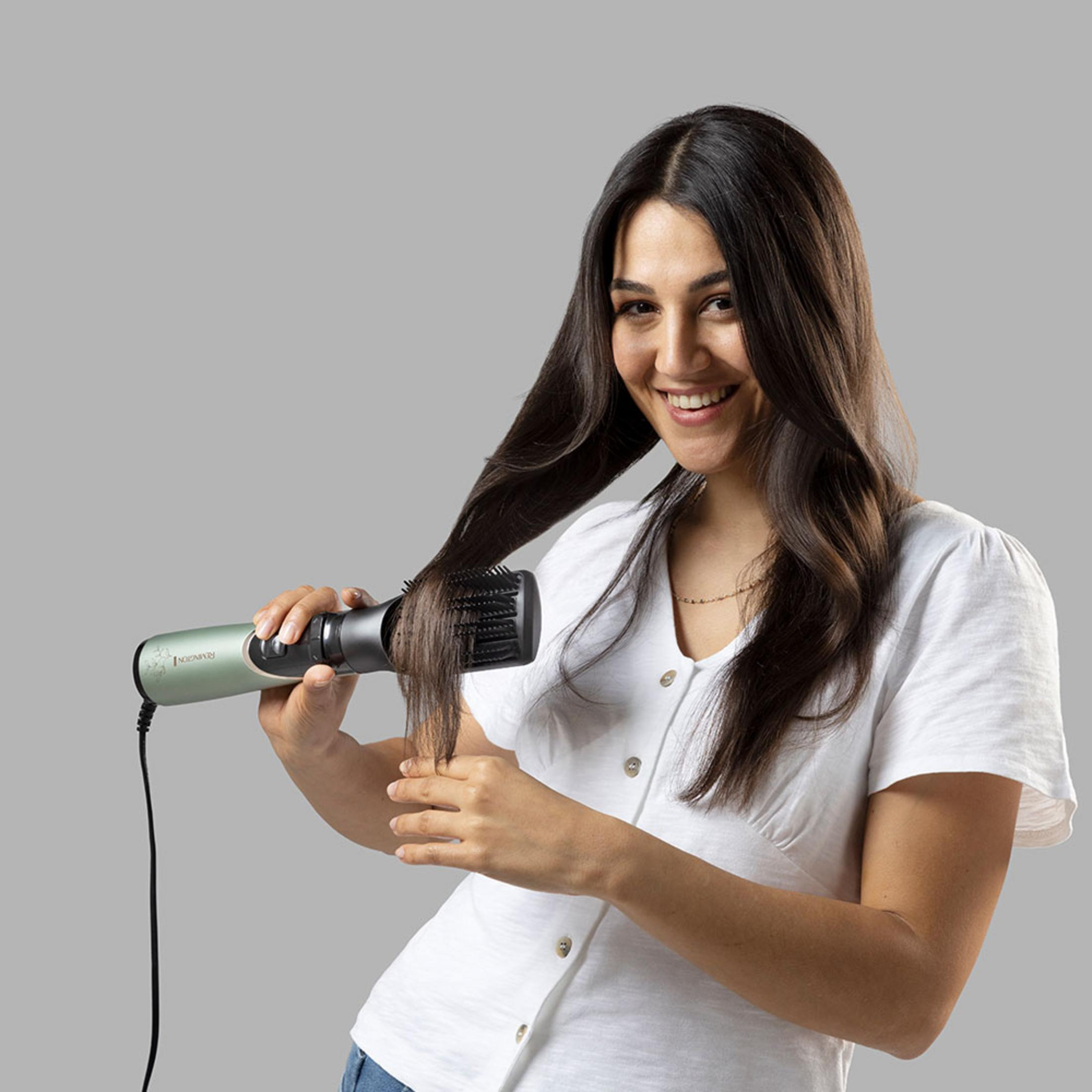 Kobieta z długimi brązowymi włosami używa zielonej szczotki do suszarki.