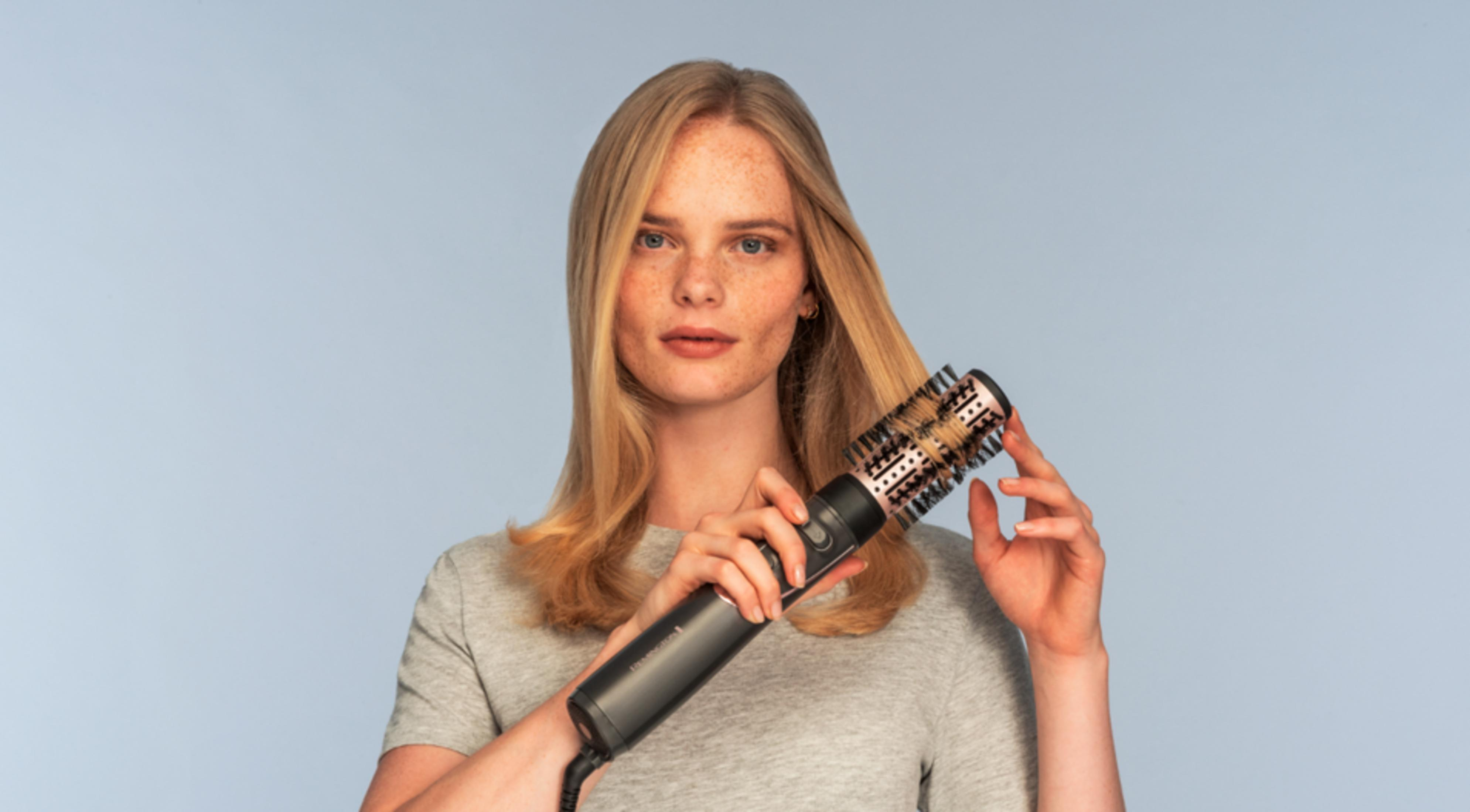 Blondynka z piegami używa obrotowej szczotki do włosów.