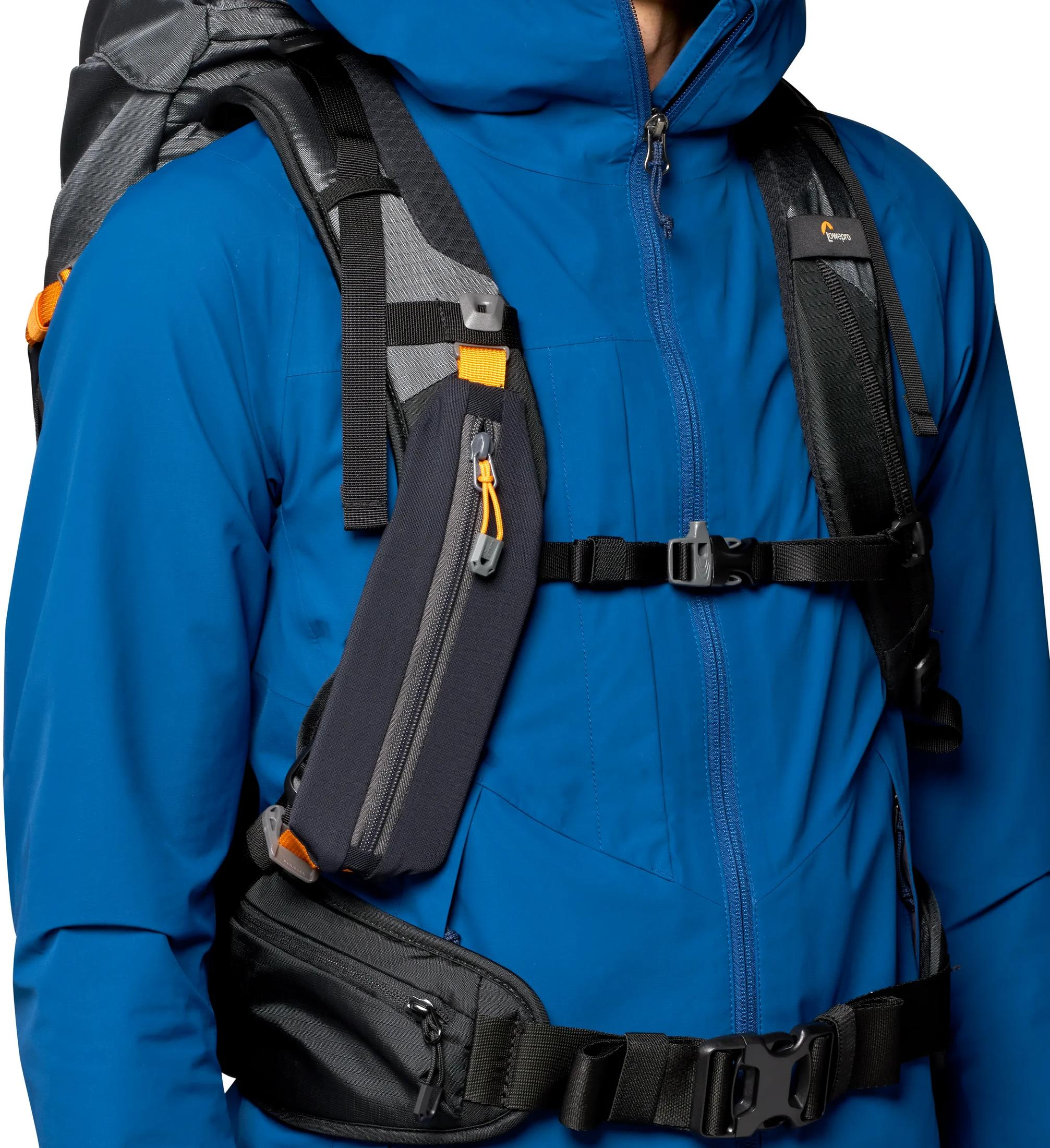 Personne en veste bleue avec sac à dos et sacs de ceinture. Accents gris et orange.