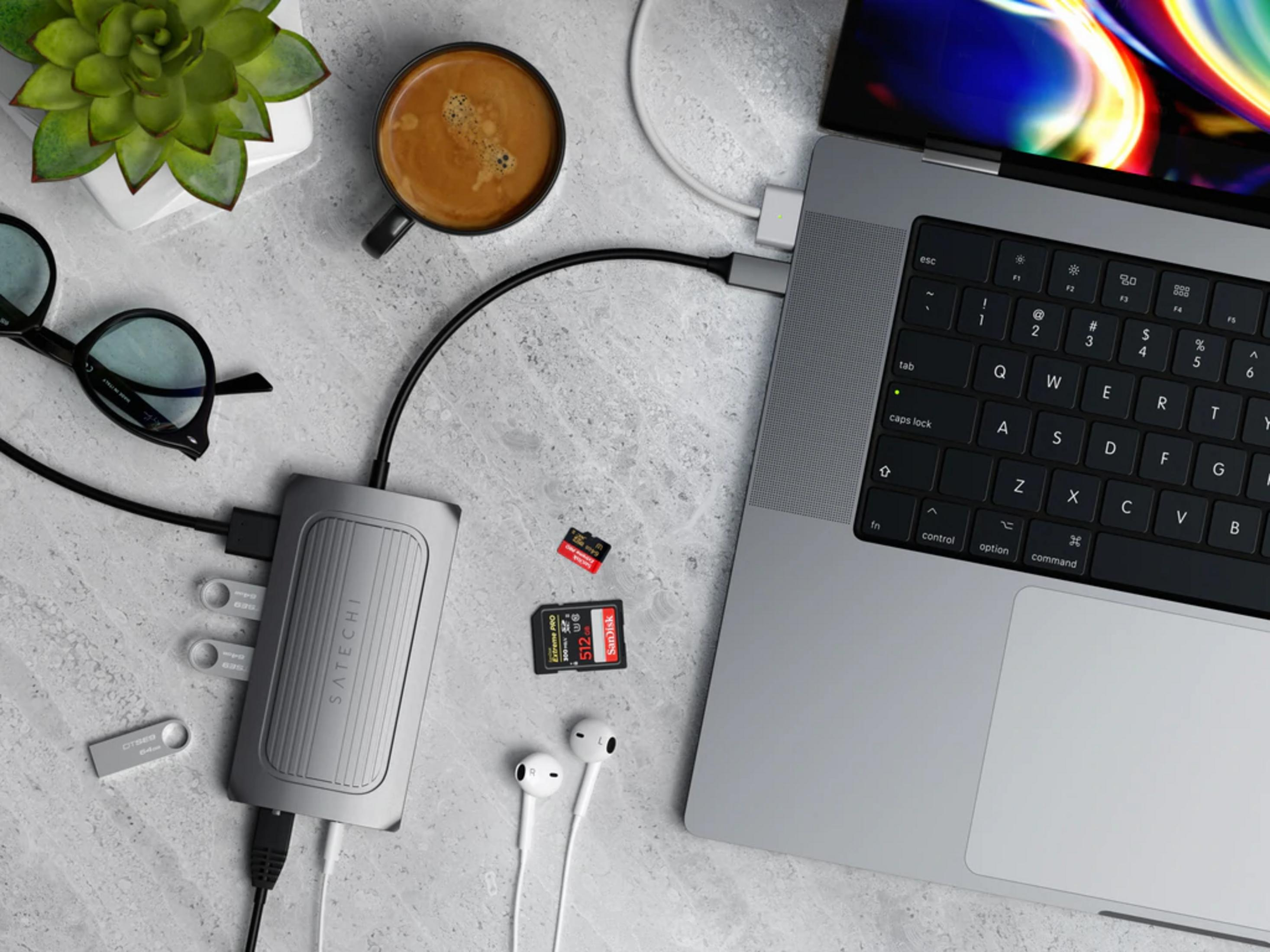Ein Laptop mit Zubehör: Kaffee, Pflanze, Brille, Hub, Speicherkarten und Kopfhörer.
