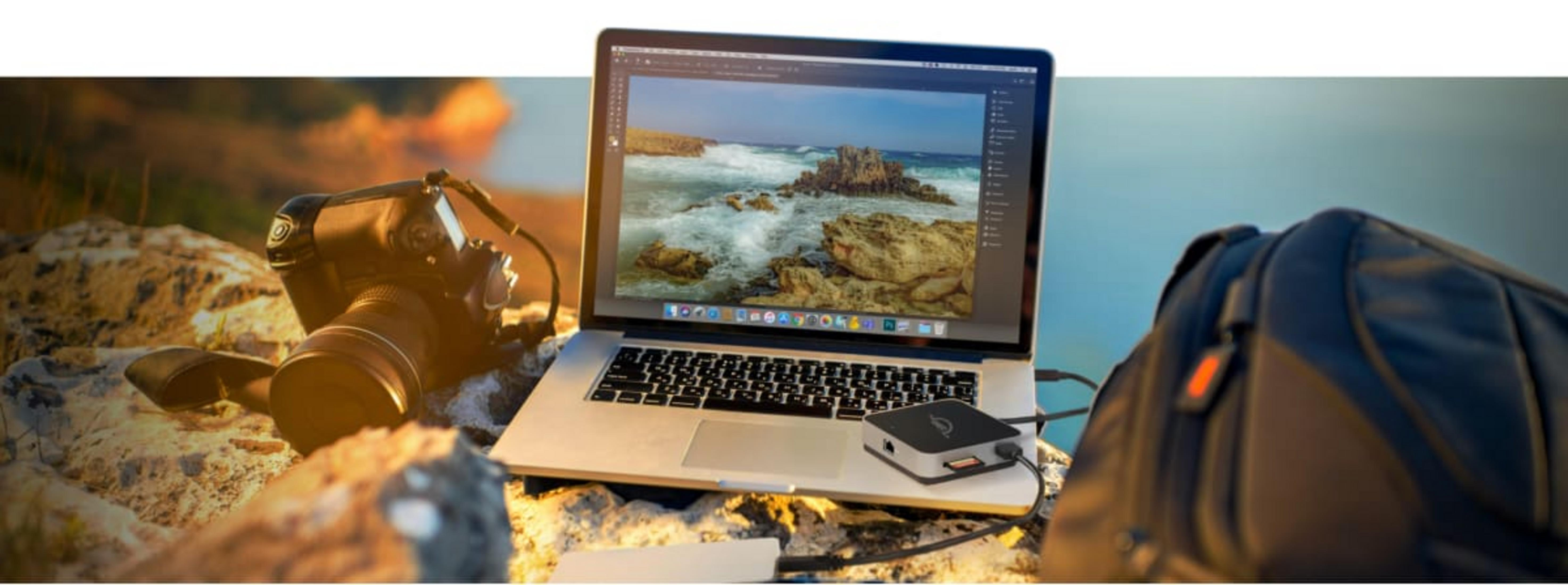 Camera, laptop met zeeafbeelding en tas op rotsen.