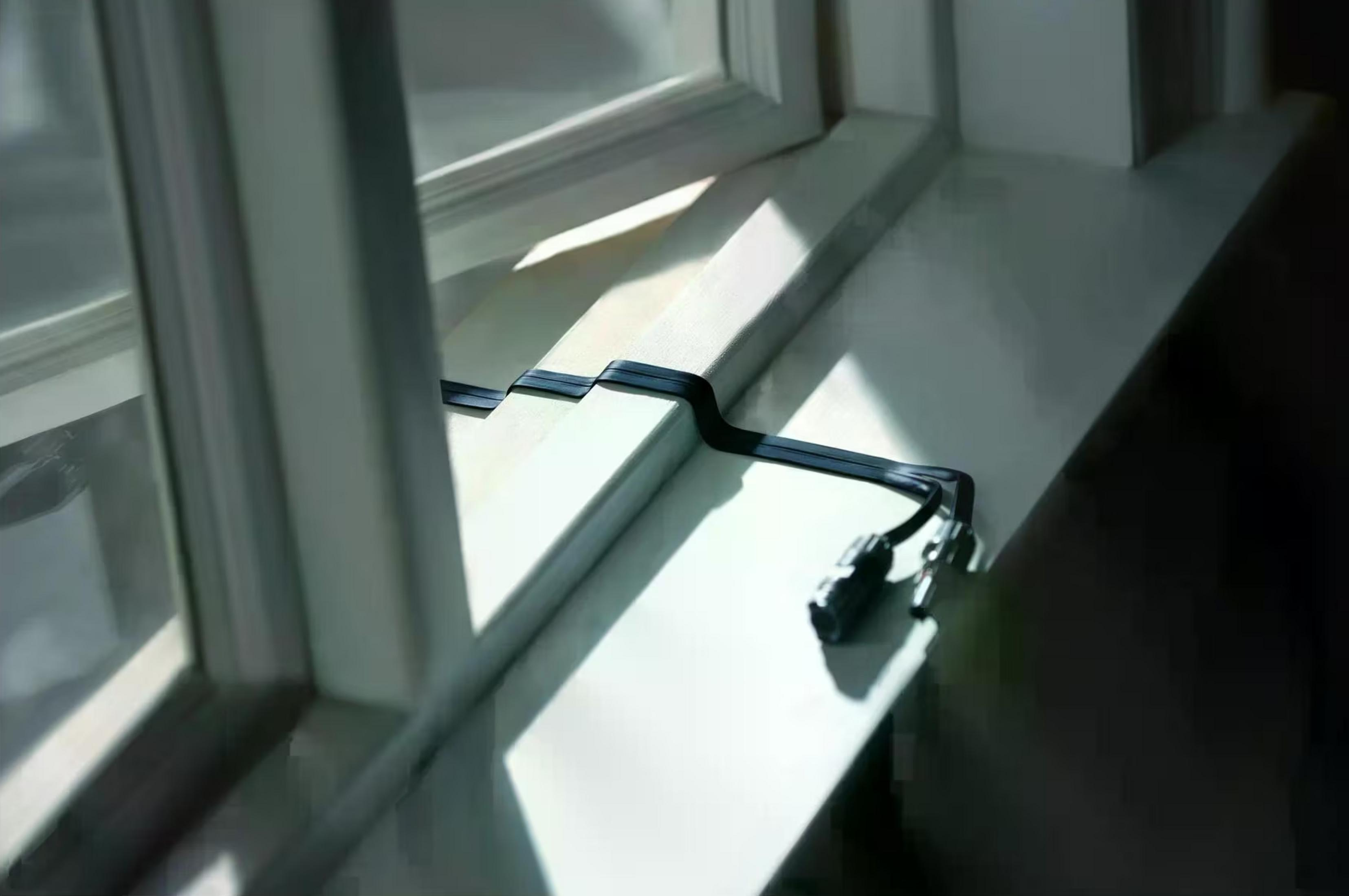 Czarny kabel z wtyczkami leży na białym parapecie w słońcu.
